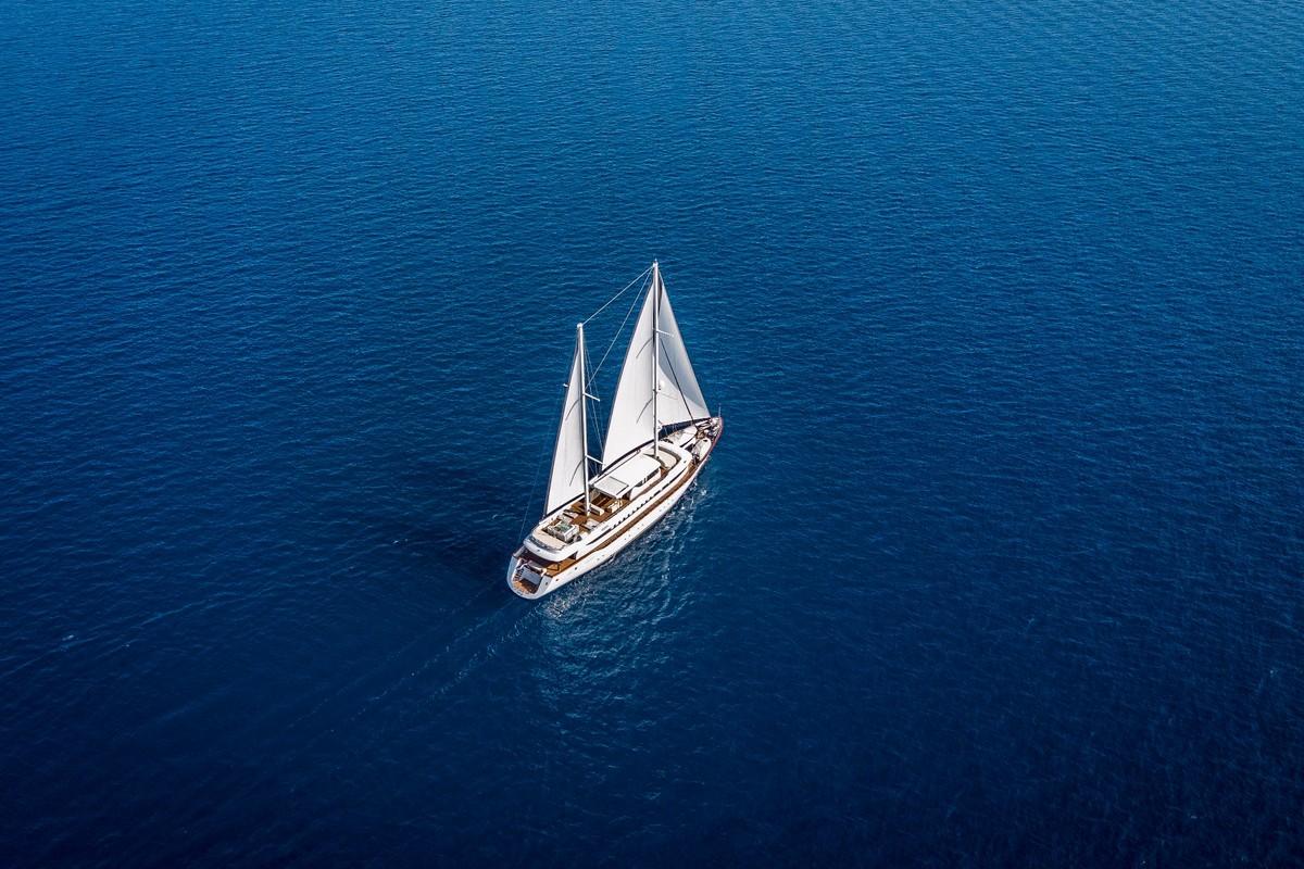 Aerial view of white sailing yacht with two sails raised on deep blue ocean