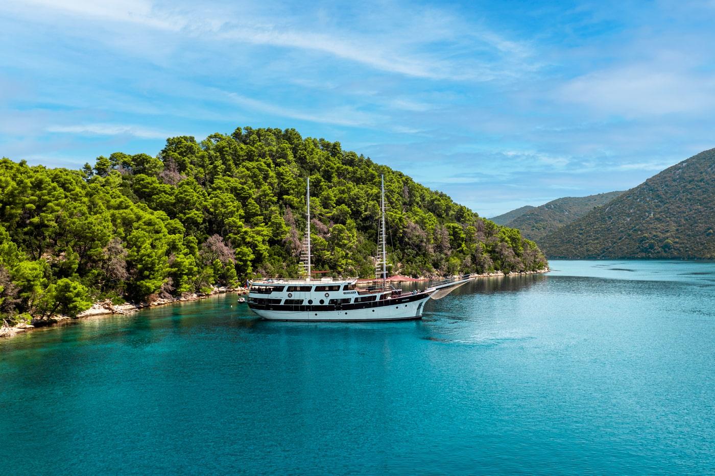 luxury white gulet yacht anchored in crystal turquoise waters near forested coastline