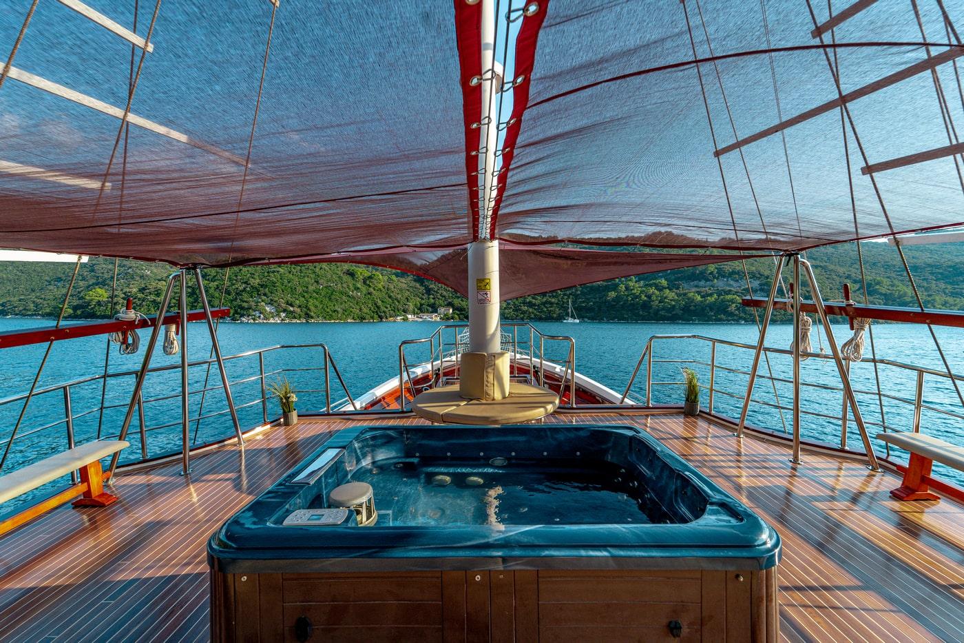 Yacht deck jacuzzi with teak flooring under sail awning overlooking forested bay