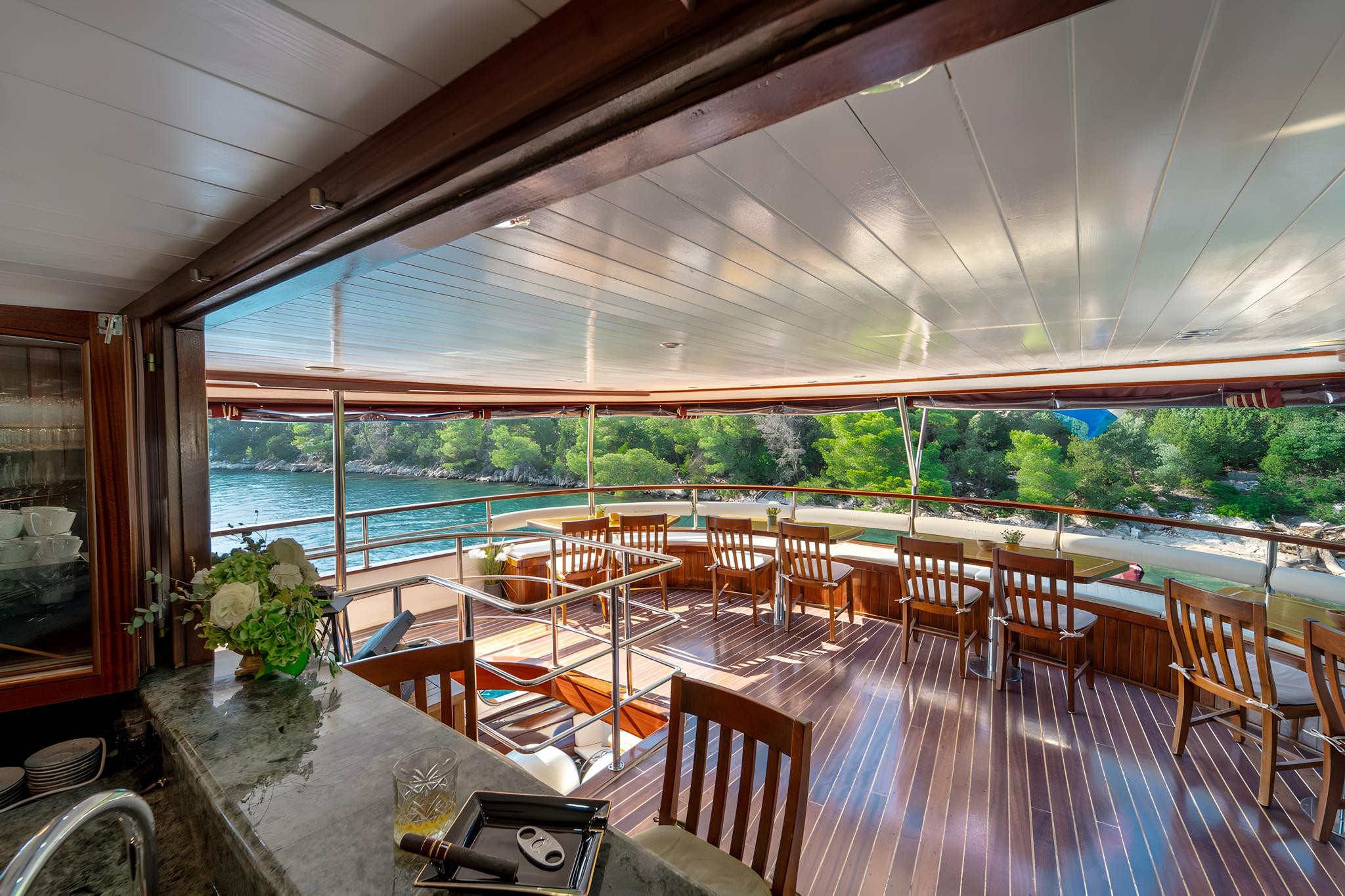 luxury yacht covered aft deck with teak dining furniture and coastal views