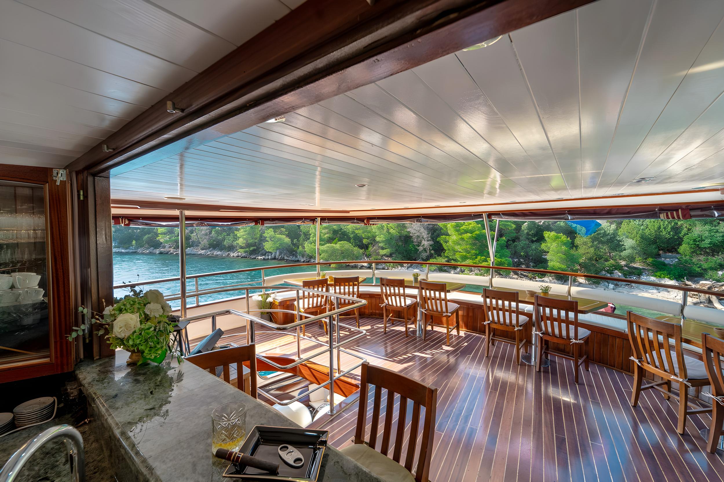 luxury yacht covered aft deck with teak dining furniture and coastal views