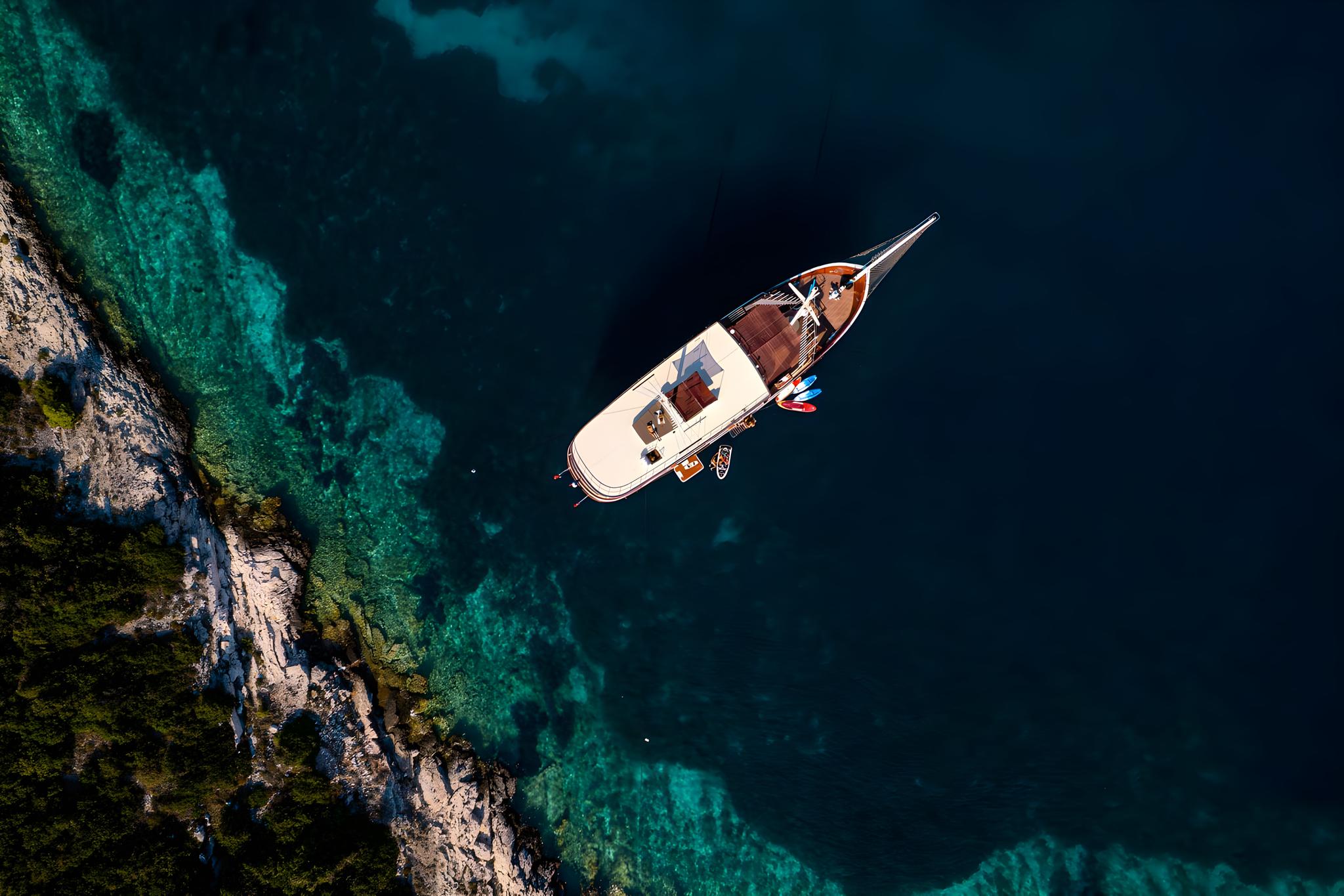 Aerial view luxury yacht anchored crystal clear turquoise waters rocky coastline