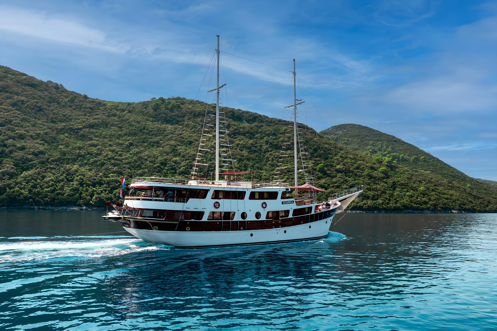 White and wood gulet yacht sailing past green hills in clear blue waters