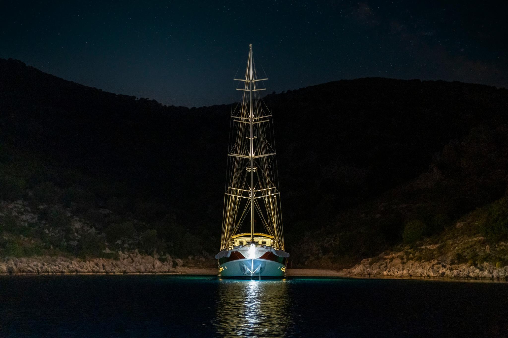 illuminated traditional sailing gulet anchored in calm bay under starry night sky