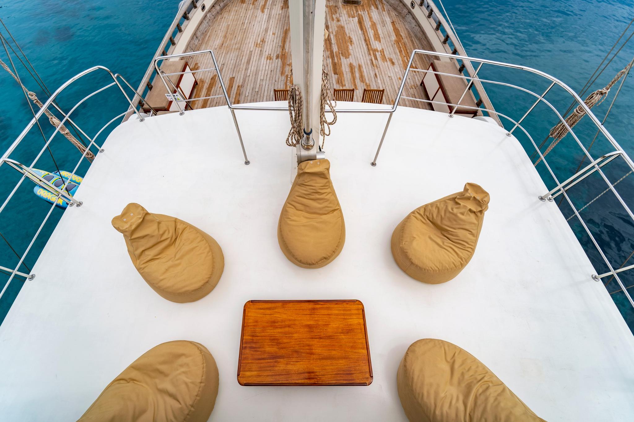 bow deck with five tan bean bag seats arranged around wooden table on white deck