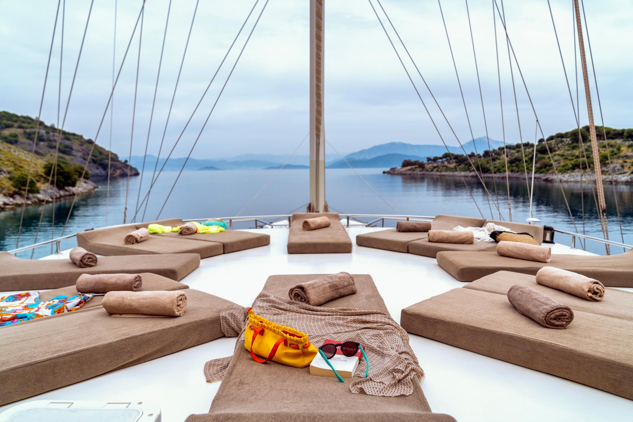 Foredeck sun lounging area with beige cushioned seating and towels arranged around mast