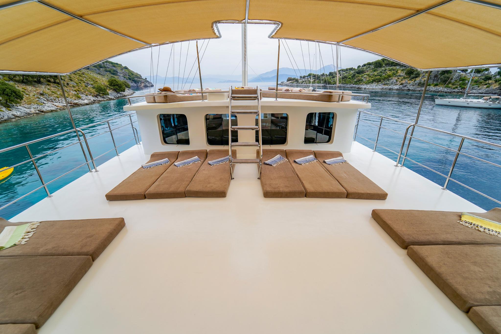 bow sun deck with brown cushioned loungers arranged under yellow awning shade