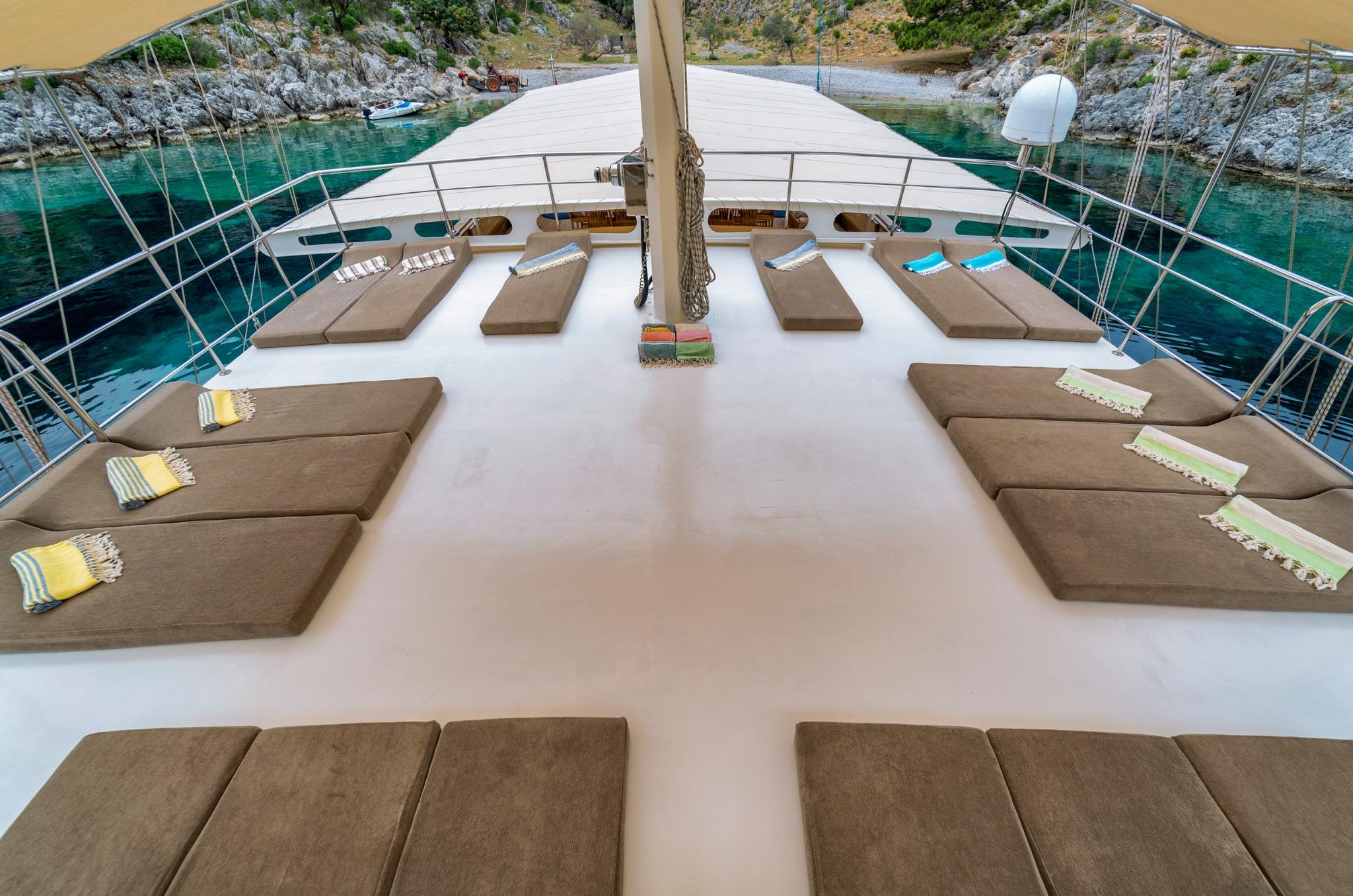 bow sun deck with symmetrically arranged taupe cushioned loungers and colorful towels overlooking turquoise bay