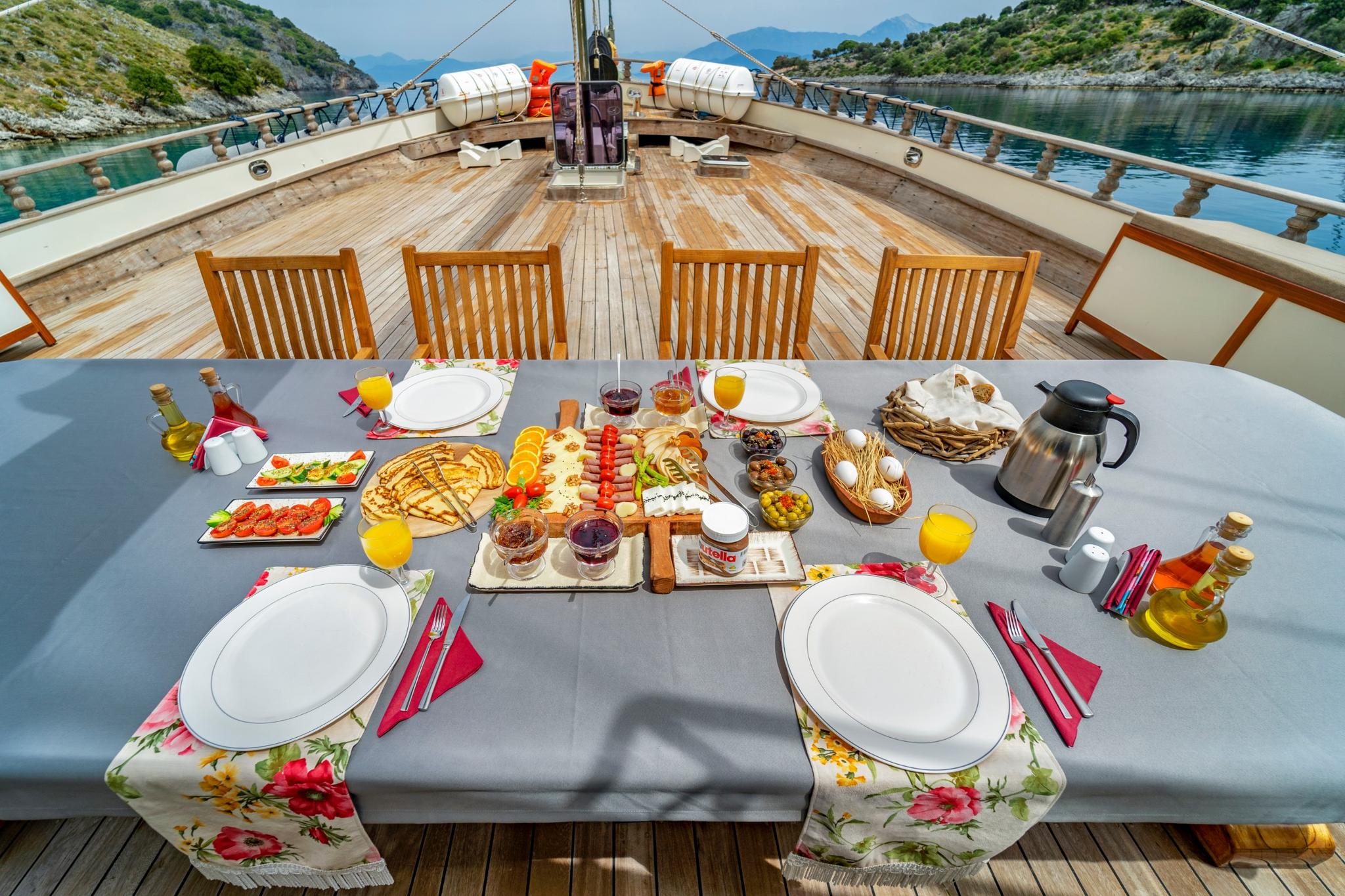 outdoor breakfast dining table with food spread, juice, bread and preserves on yacht deck