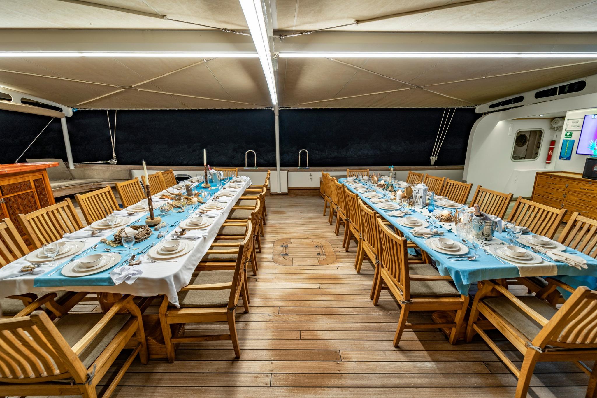 covered aft deck dining area with two formal dining tables and teak chairs