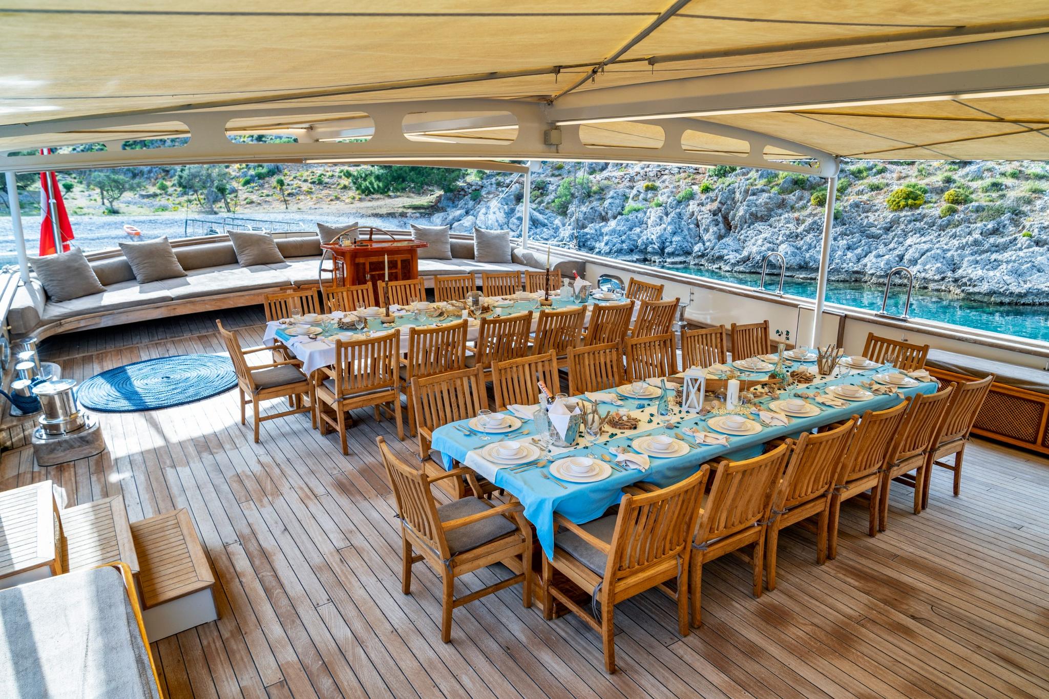 luxury yacht covered aft deck with formal dining table and teak chairs overlooking scenic coastline