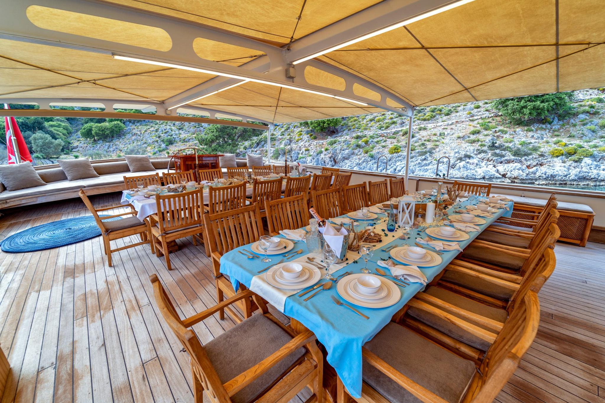 Gulet aft deck dining area with formal table setting under beige awning