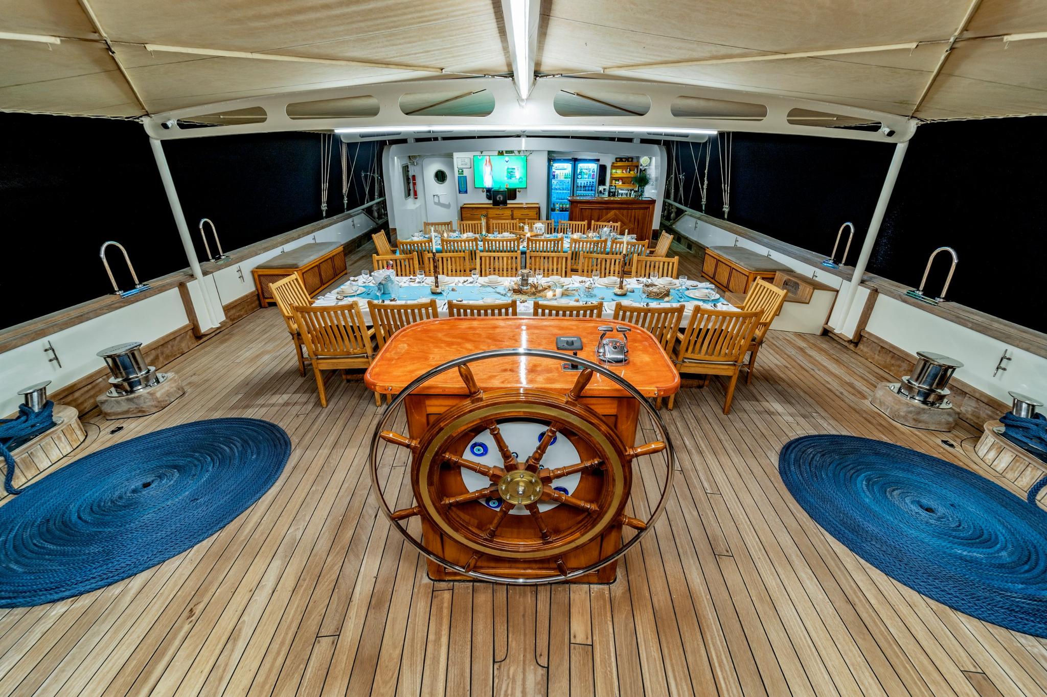 yacht aft deck with formal dining table, traditional ship's wheel, and teak decking