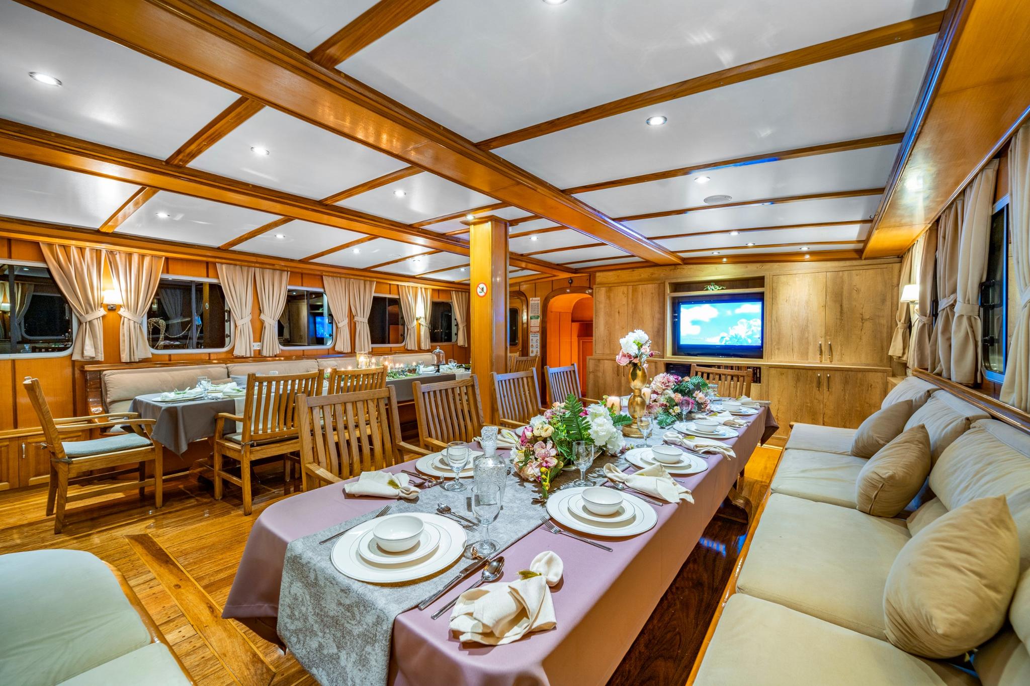 luxury yacht main salon with formal dining table, wooden beams, and entertainment screen