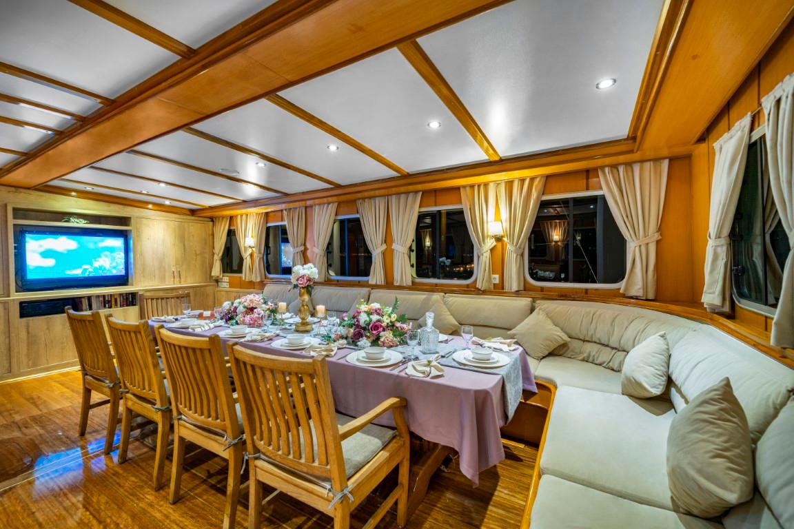 yacht interior dining salon with formal table setting, cream banquette seating, wooden chairs and wall-mounted television