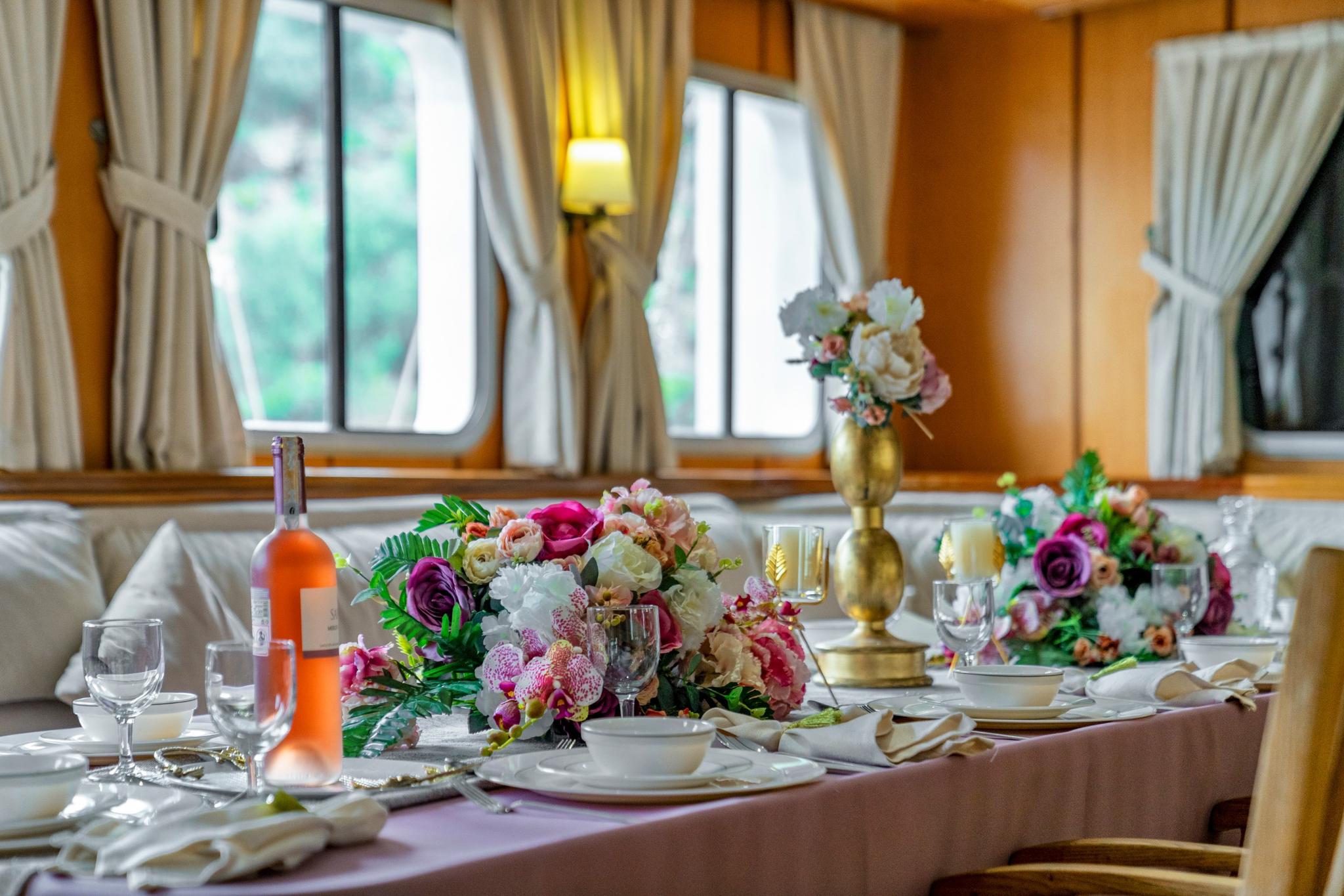 elegant yacht dining salon with formal table setting, floral centerpieces and wine bottle