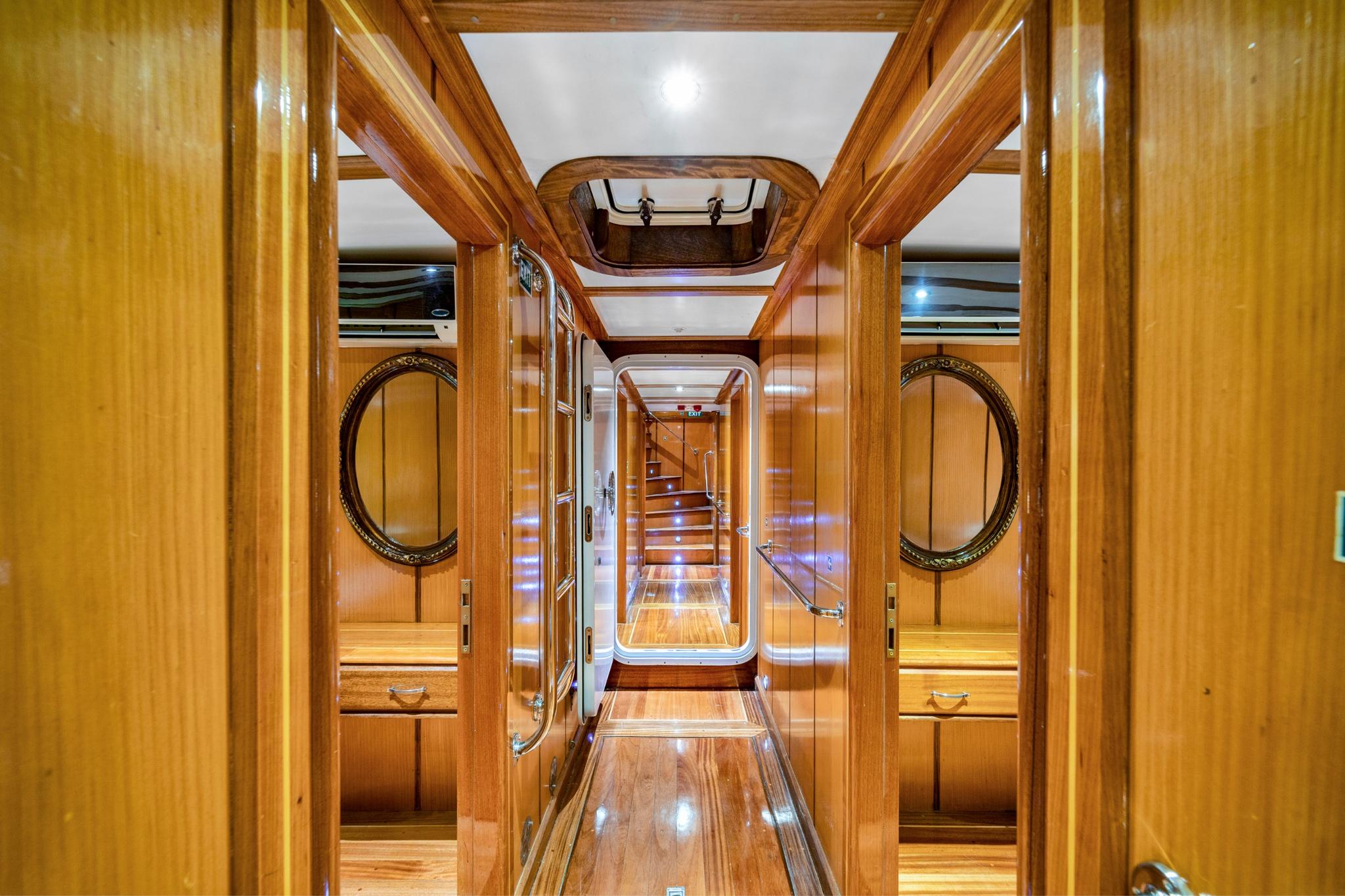 luxury yacht interior corridor with polished wood paneling, round porthole windows, and cabin doors