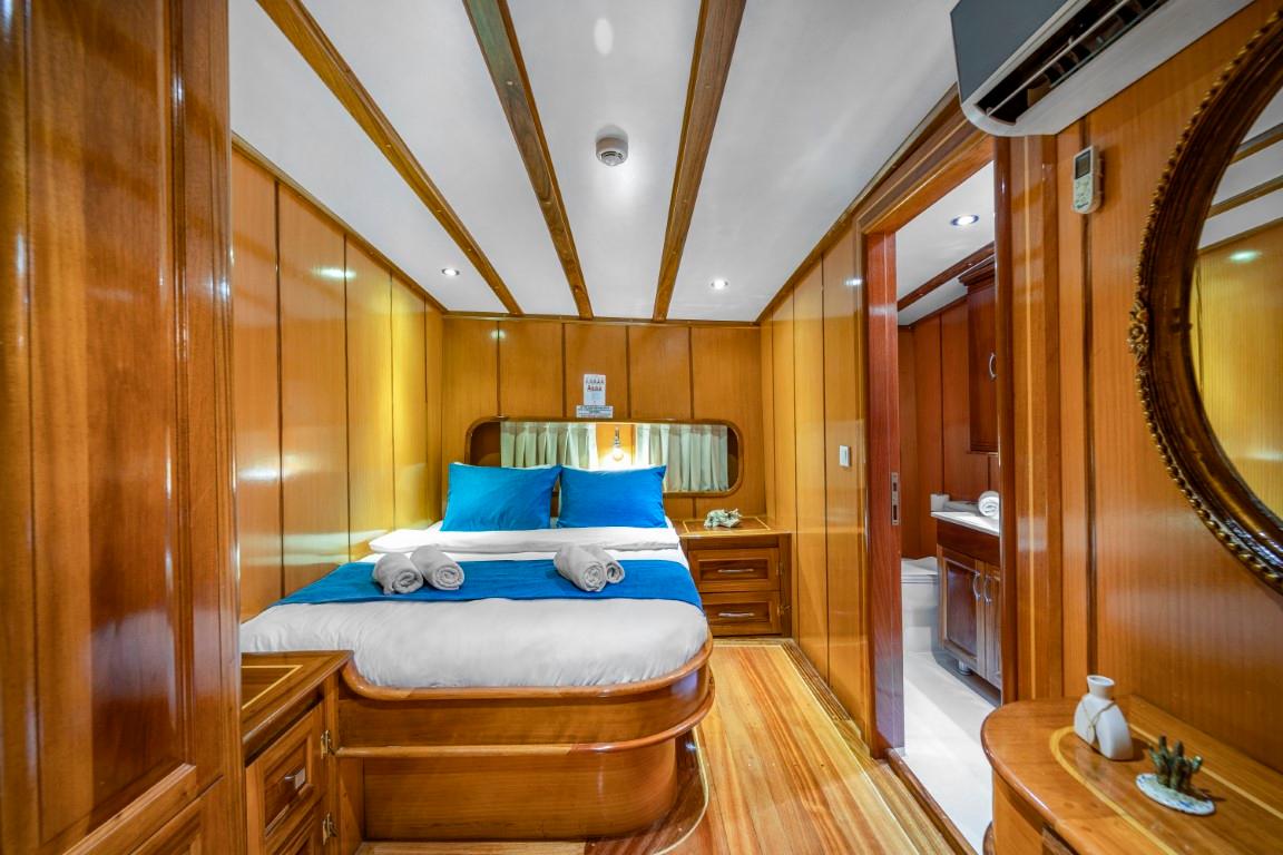 yacht guest cabin featuring double bed with blue pillows, wood paneling and en-suite bathroom