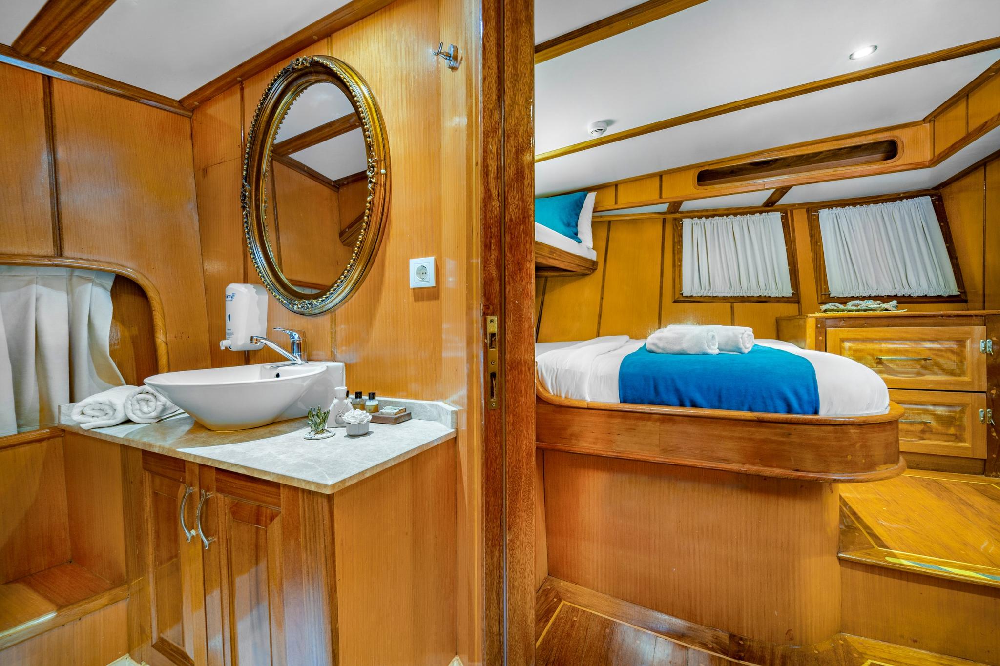 yacht cabin interior with built-in bed, vessel sink, ornate mirror and wooden paneling