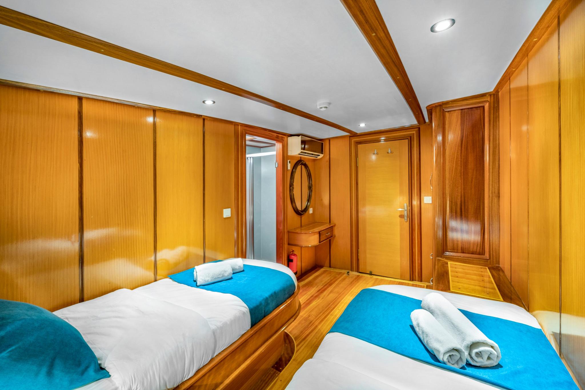 Twin cabin interior with two single beds, blue bedding, wooden paneling and built-in vanity