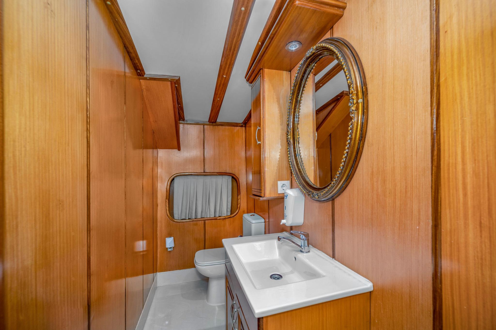 yacht guest bathroom with white sink, ornate oval mirror, and honey wood paneling