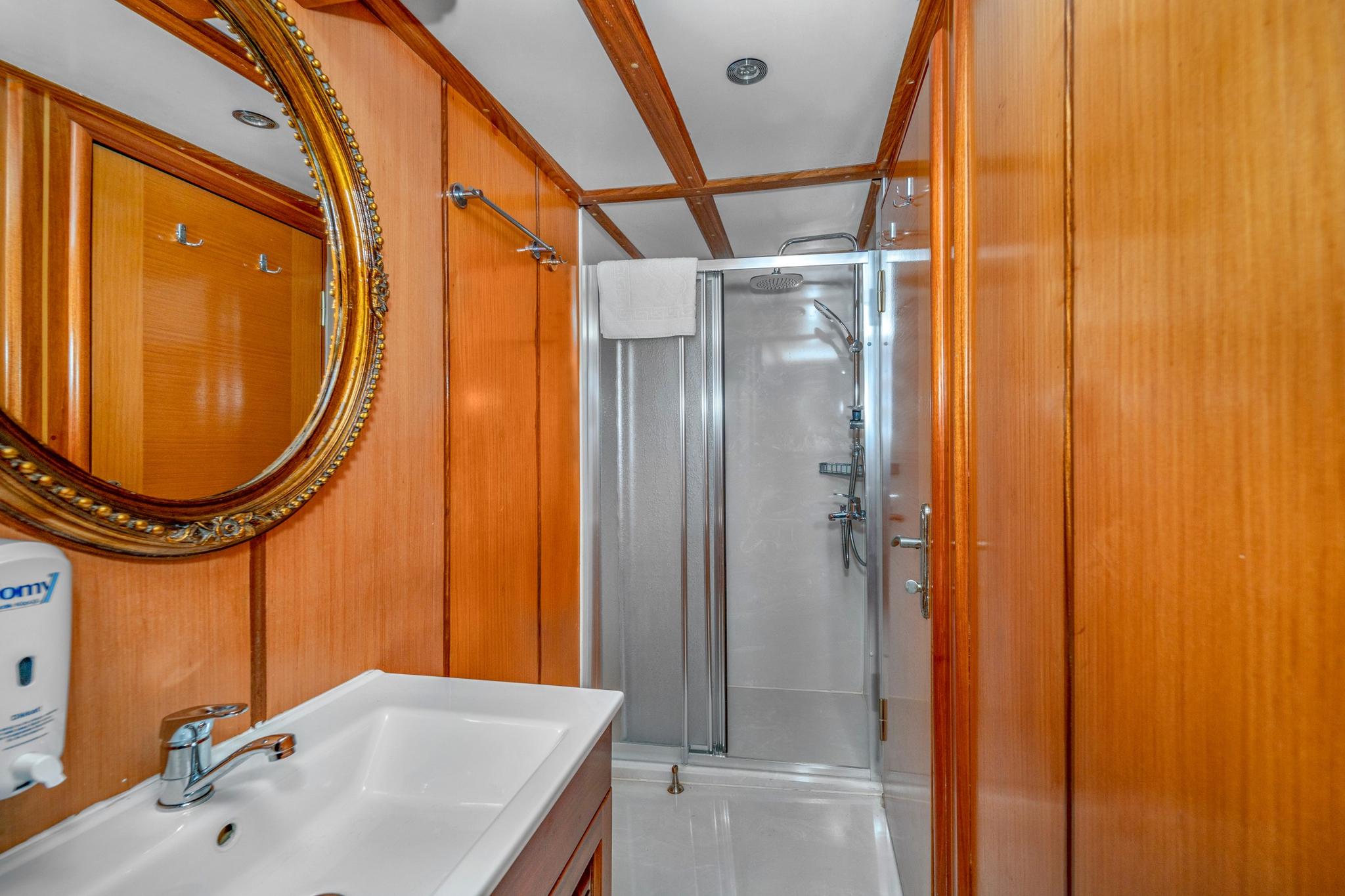 yacht bathroom featuring glass shower enclosure, ornate mirror, and warm wood paneling