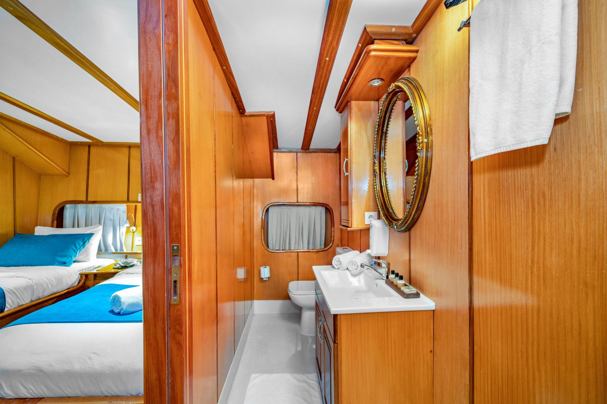 yacht guest cabin showing single bed with blue bedding and adjoining en-suite bathroom with mirror