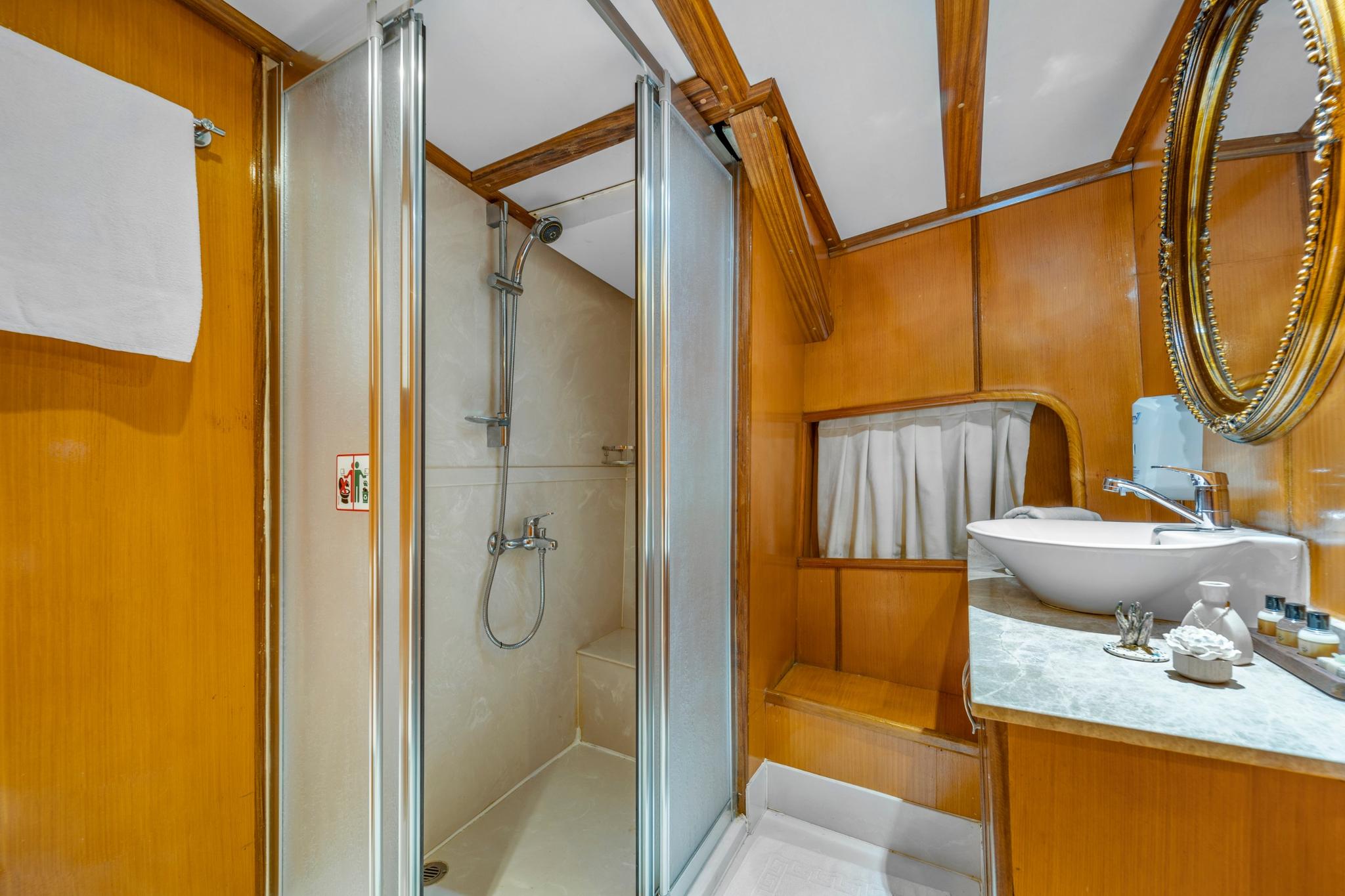 yacht bathroom featuring glass shower cabin, white vessel sink on marble countertop, and warm wood paneling