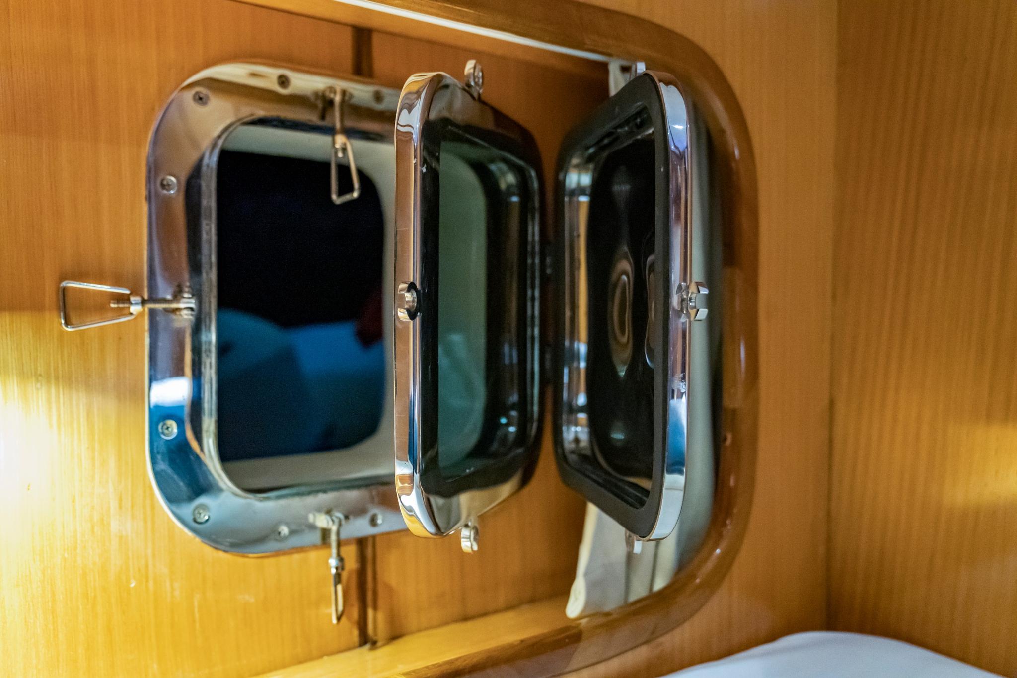 yacht cabin porthole window with chrome hinged frame in wooden wall