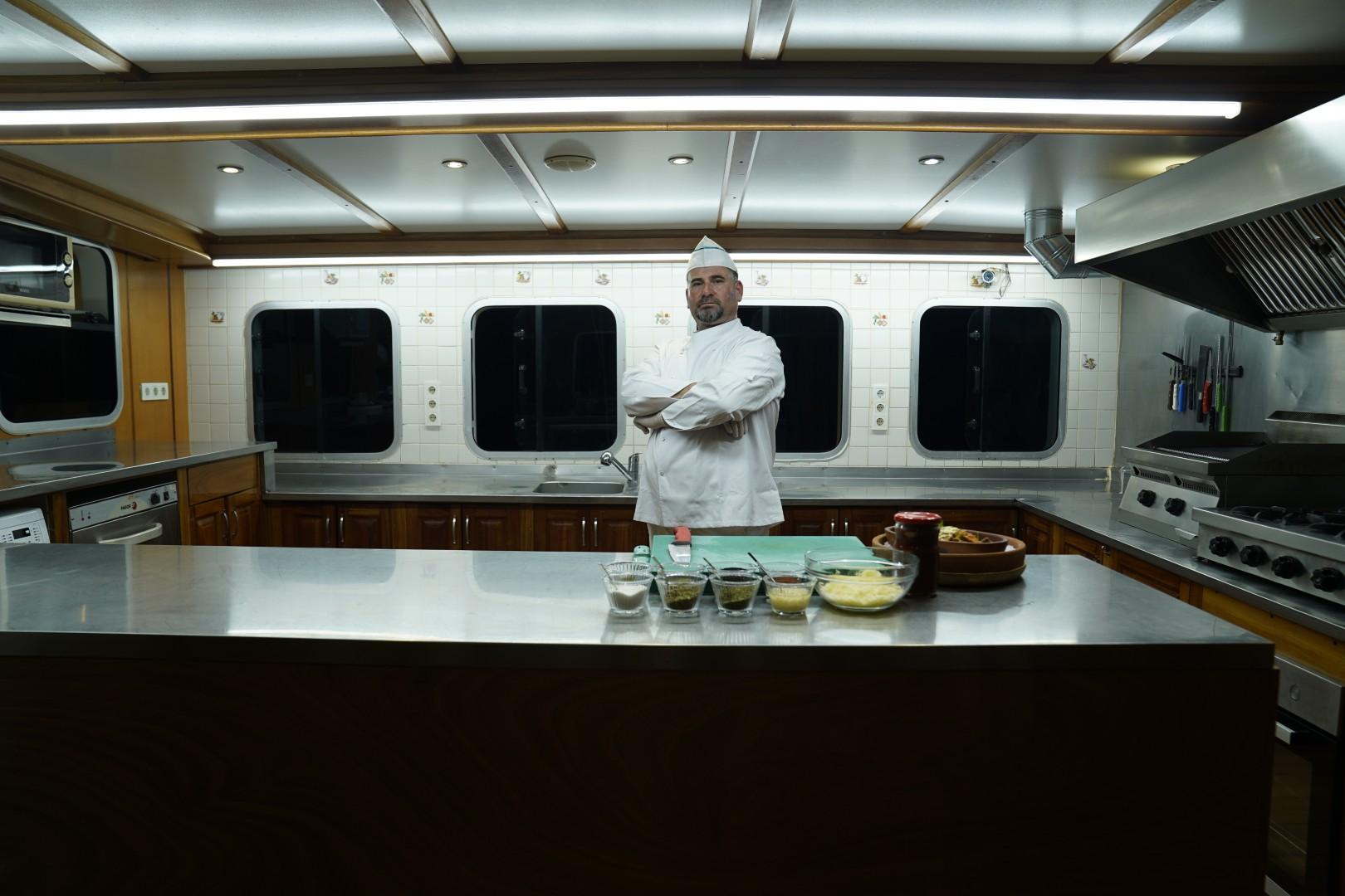 professional chef in white uniform standing in luxury yacht galley with prepared food dishes
