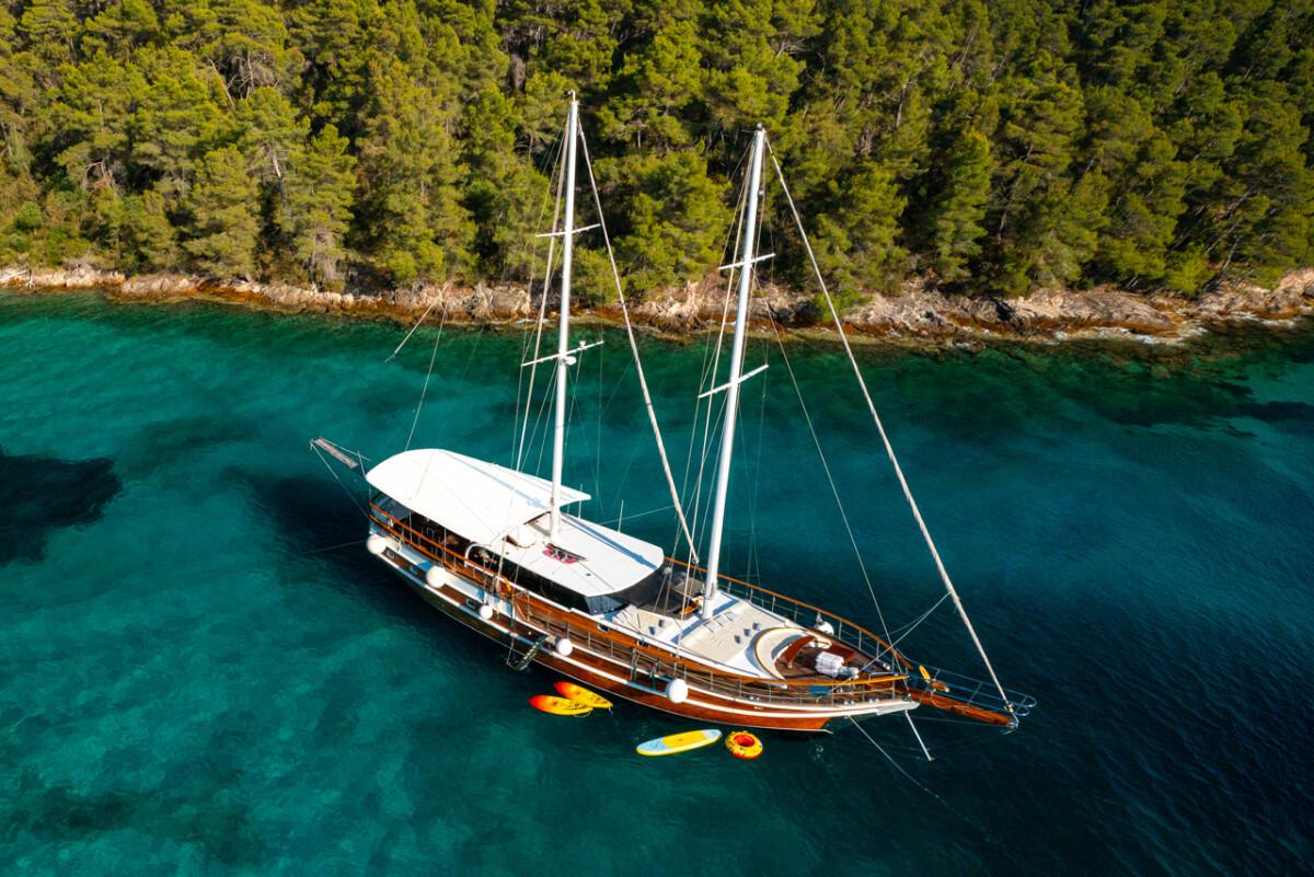 Traditional wooden gulet yacht with two masts anchored in crystal clear turquoise waters