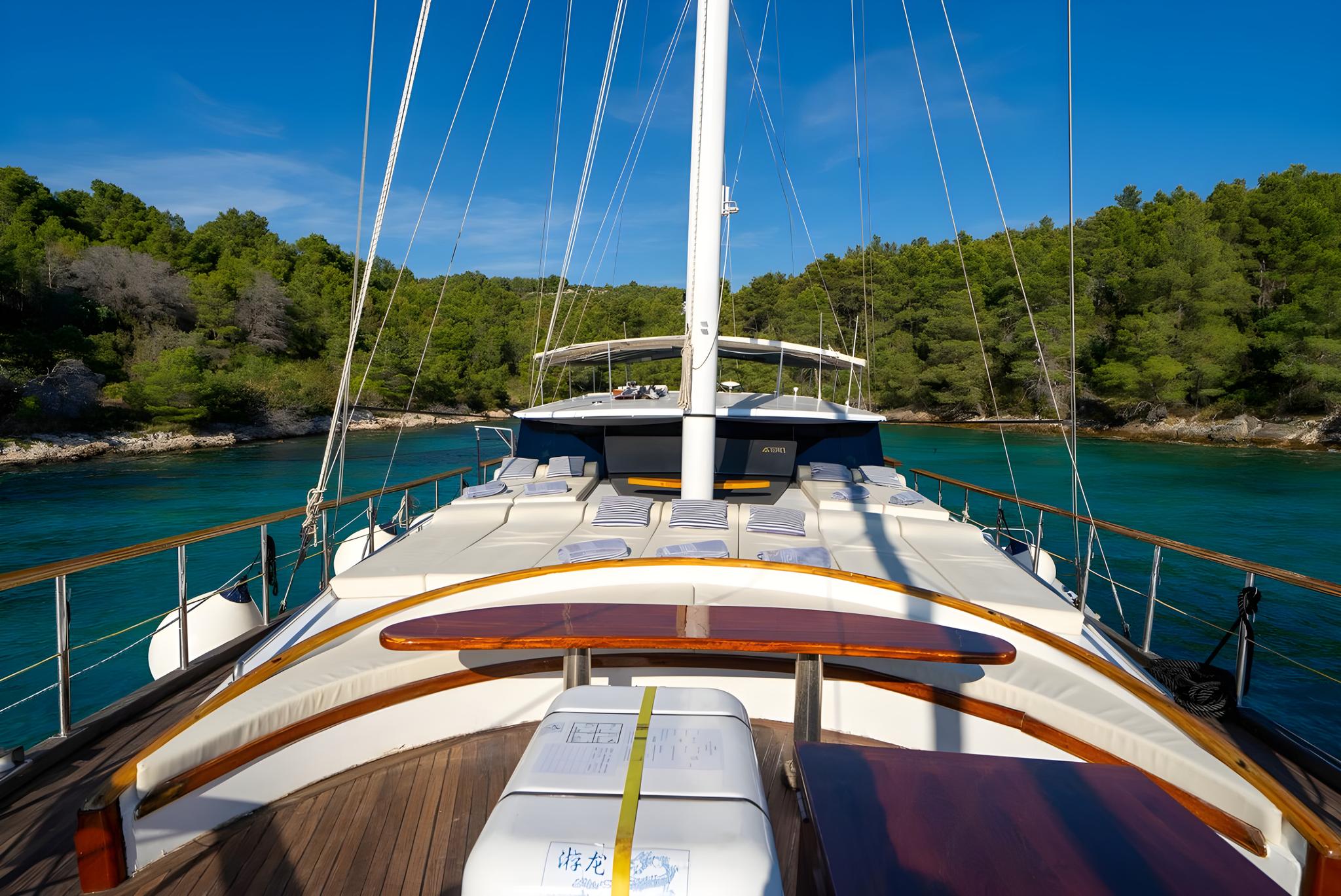 Sailing yacht bow deck with white cushioned seating in turquoise bay
