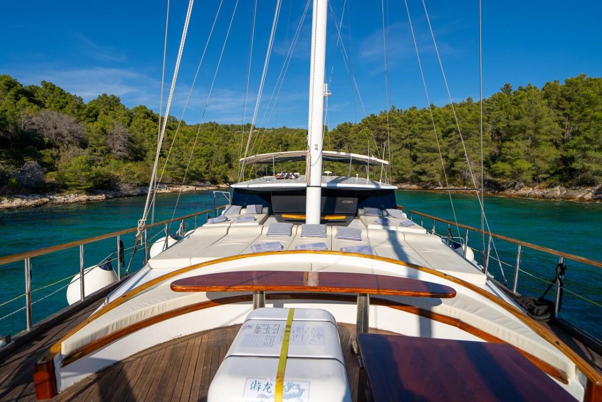 Sailing yacht bow deck with white cushioned seating in turquoise bay