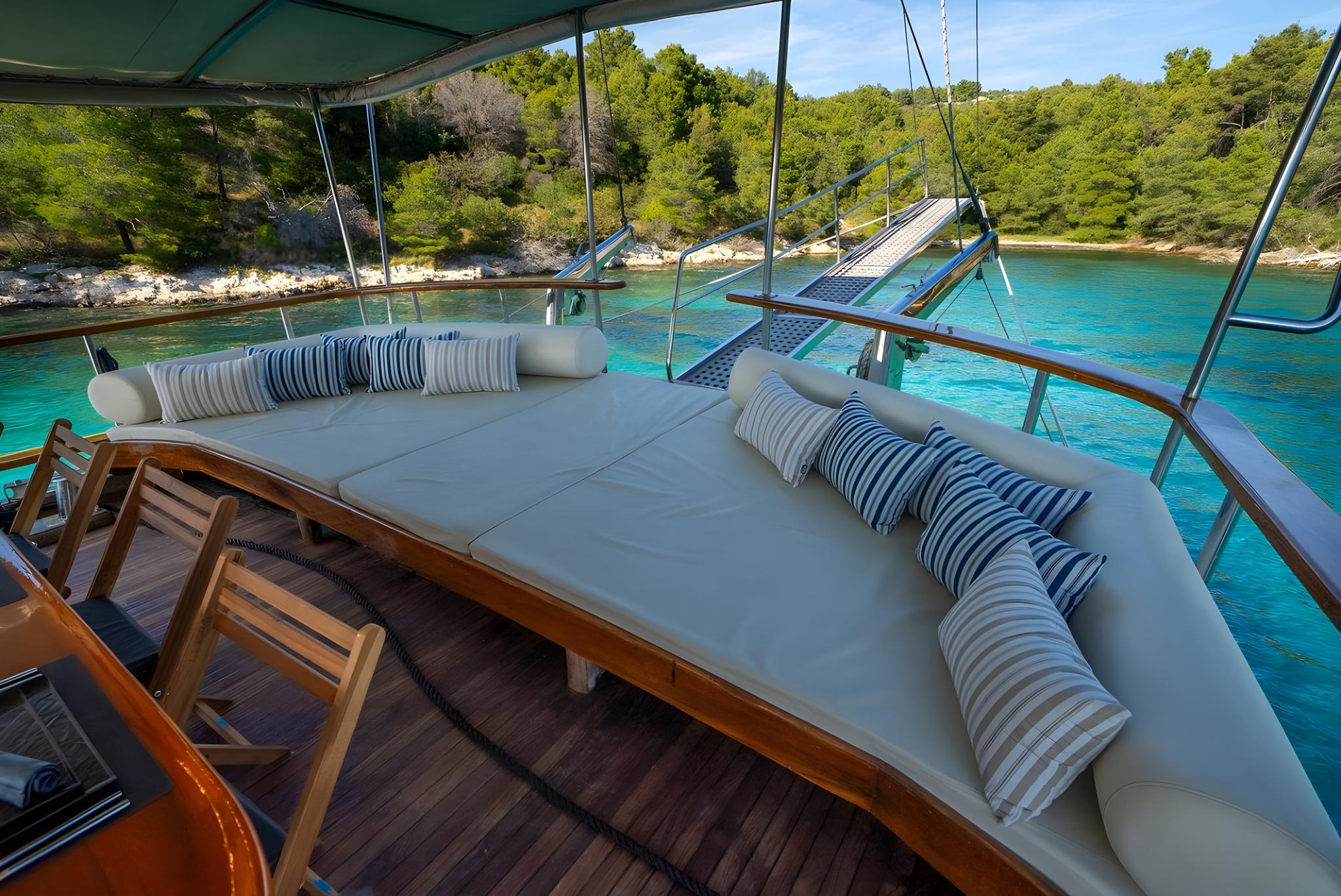 yacht covered deck seating area with white cushions overlooking turquoise bay
