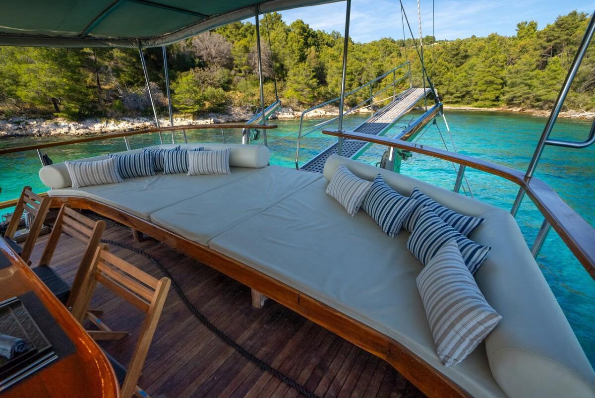 yacht covered deck seating area with white cushions overlooking turquoise bay