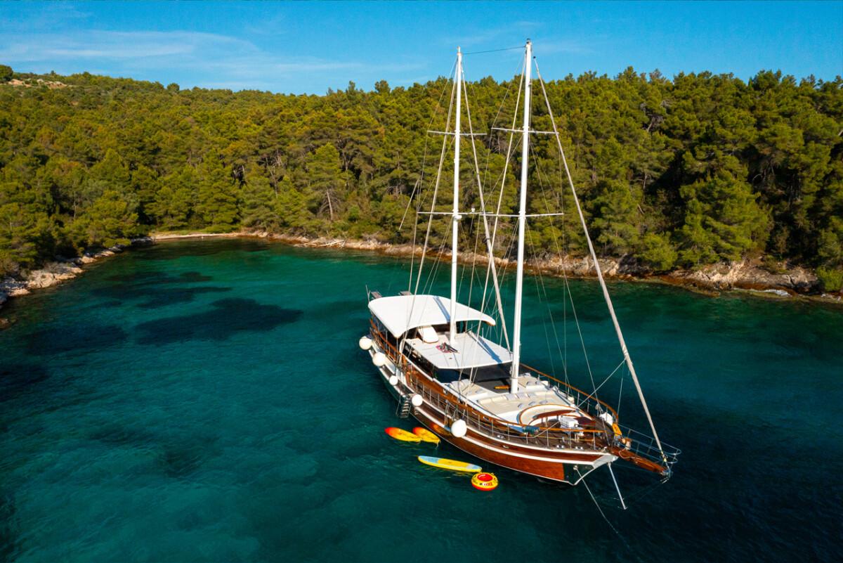 Aerial view of traditional wooden gulet yacht anchored in crystal clear turquoise bay