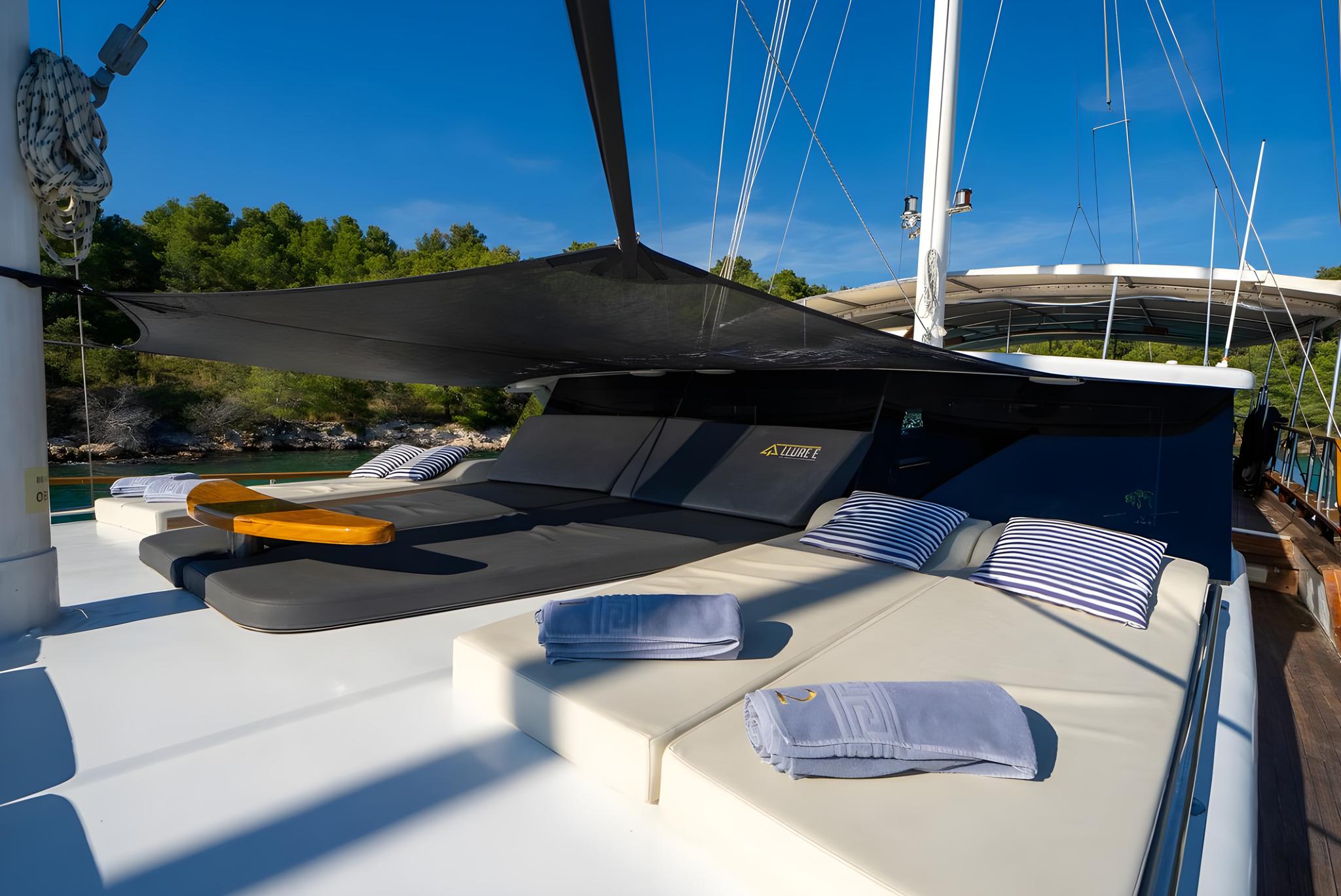 Gulet forward deck sunbeds with black shade sail and striped cushions
