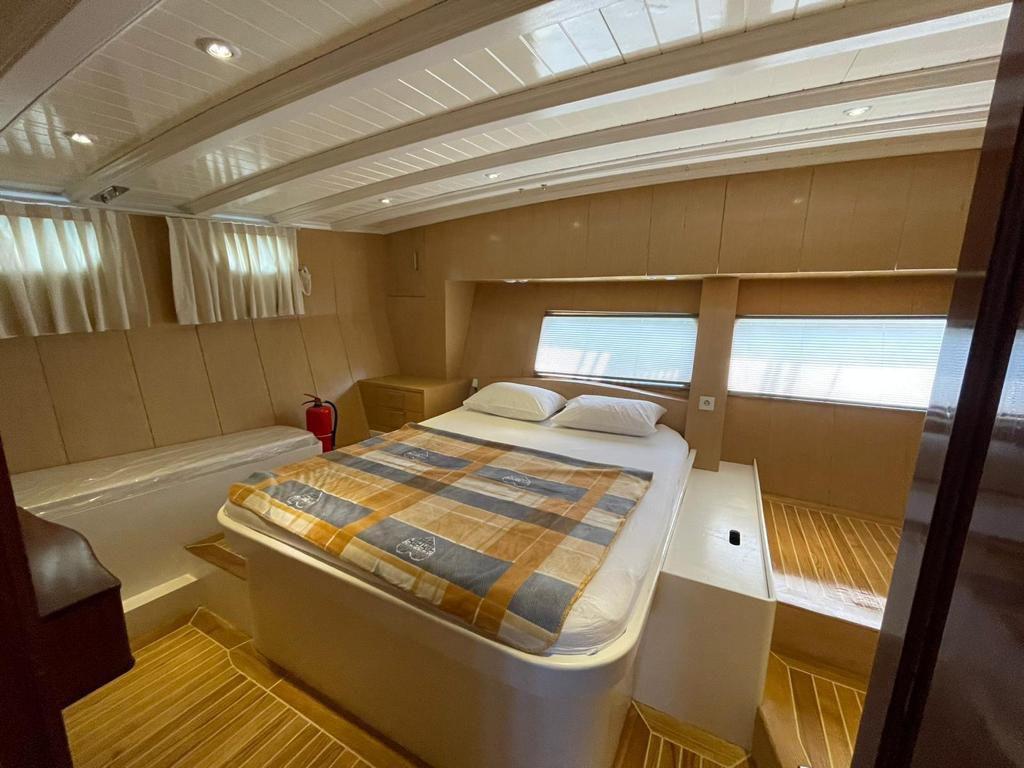 yacht cabin interior with white double bed, wooden paneling, porthole windows and teak flooring