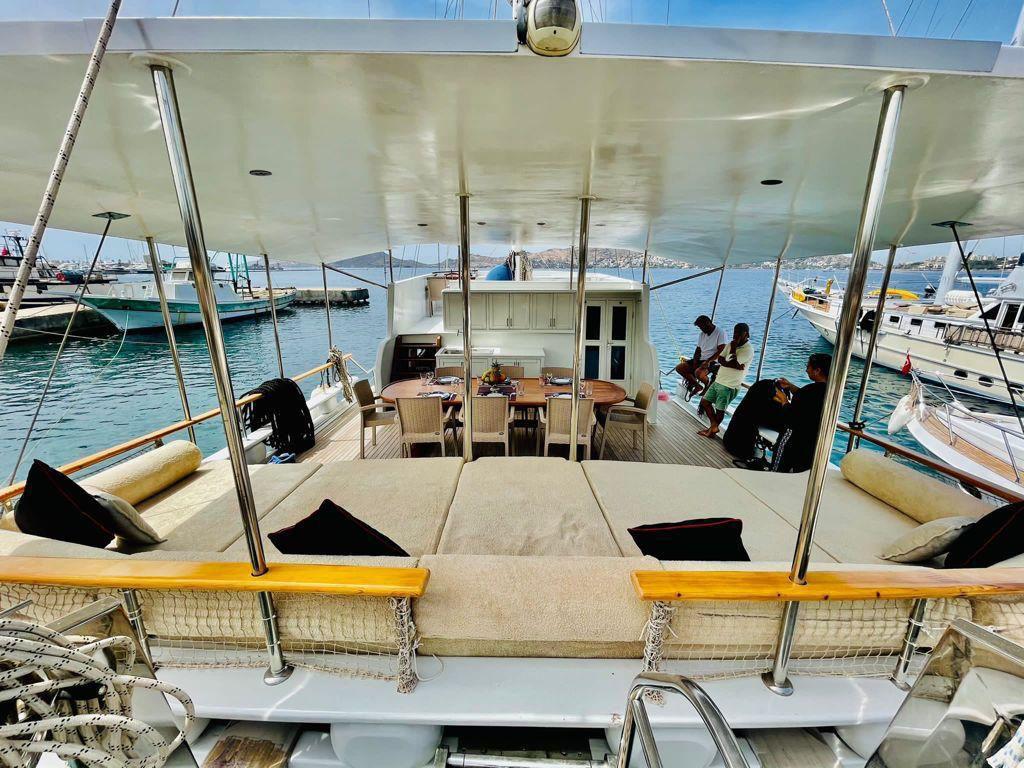 gulet aft deck with cushioned seating area, dining table and white wheelhouse structure
