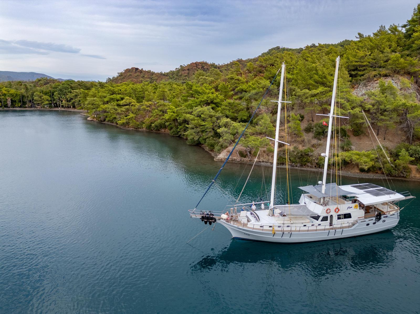 aerial view of white traditional gulet yacht anchored in turquoise bay surrounded by forested coastline