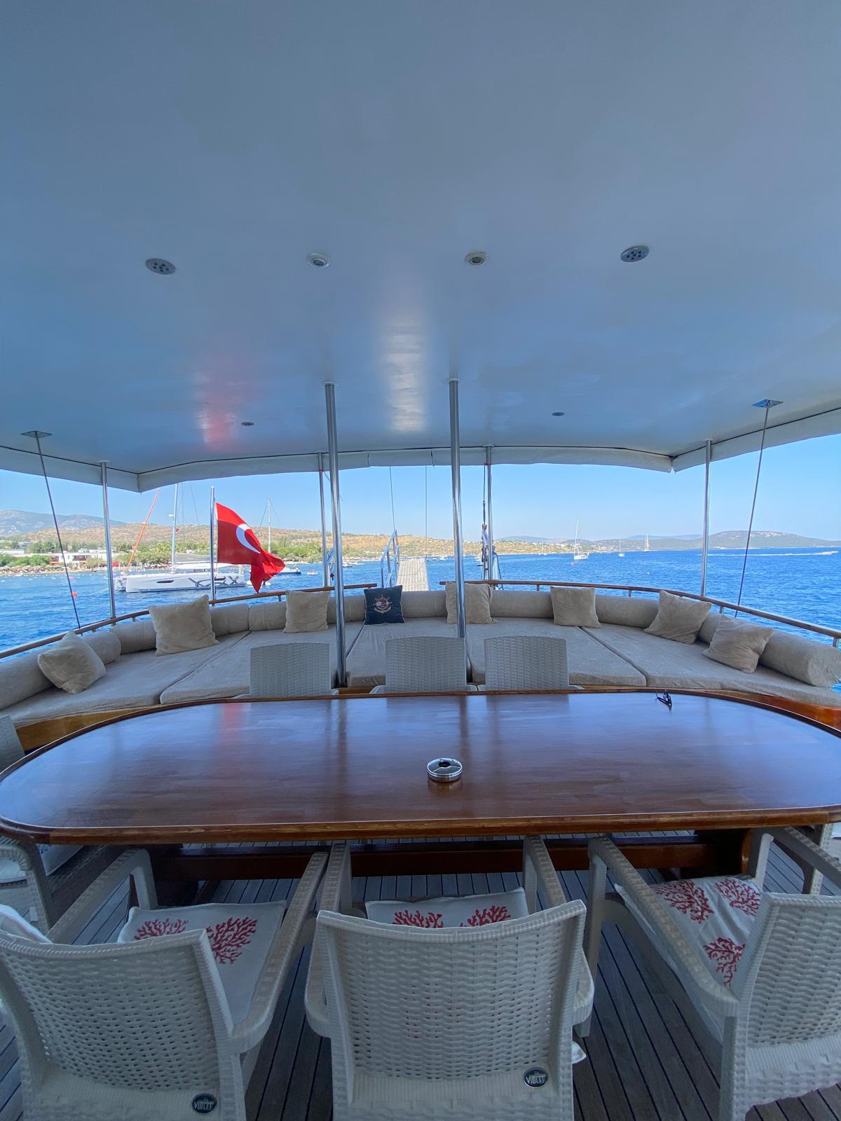 Gulet aft deck with curved banquette seating, oval dining table and Turkish flag