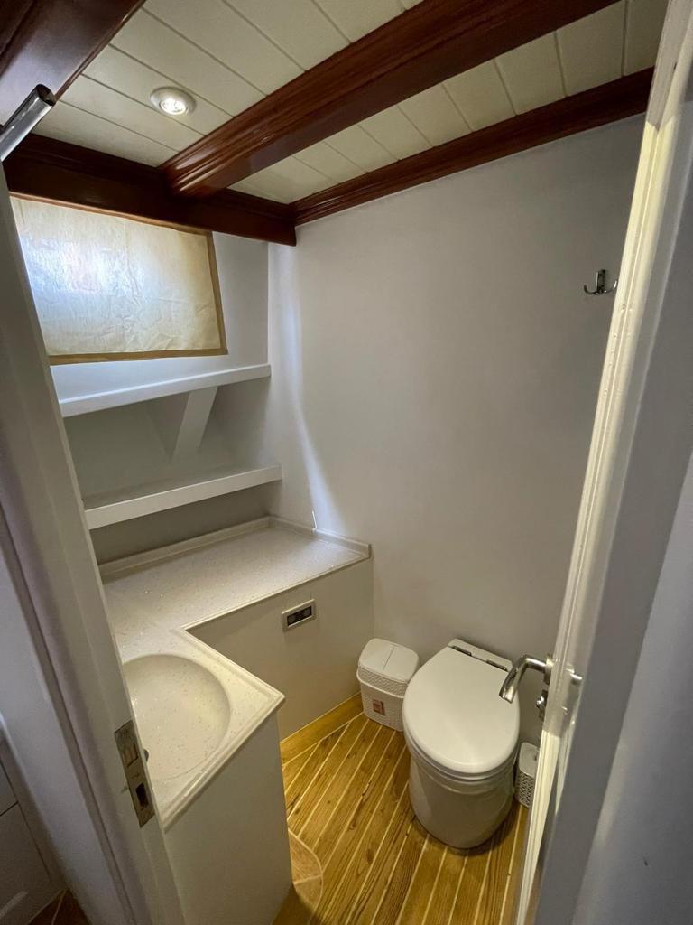 small yacht bathroom showing toilet, white surfaces, and teak flooring
