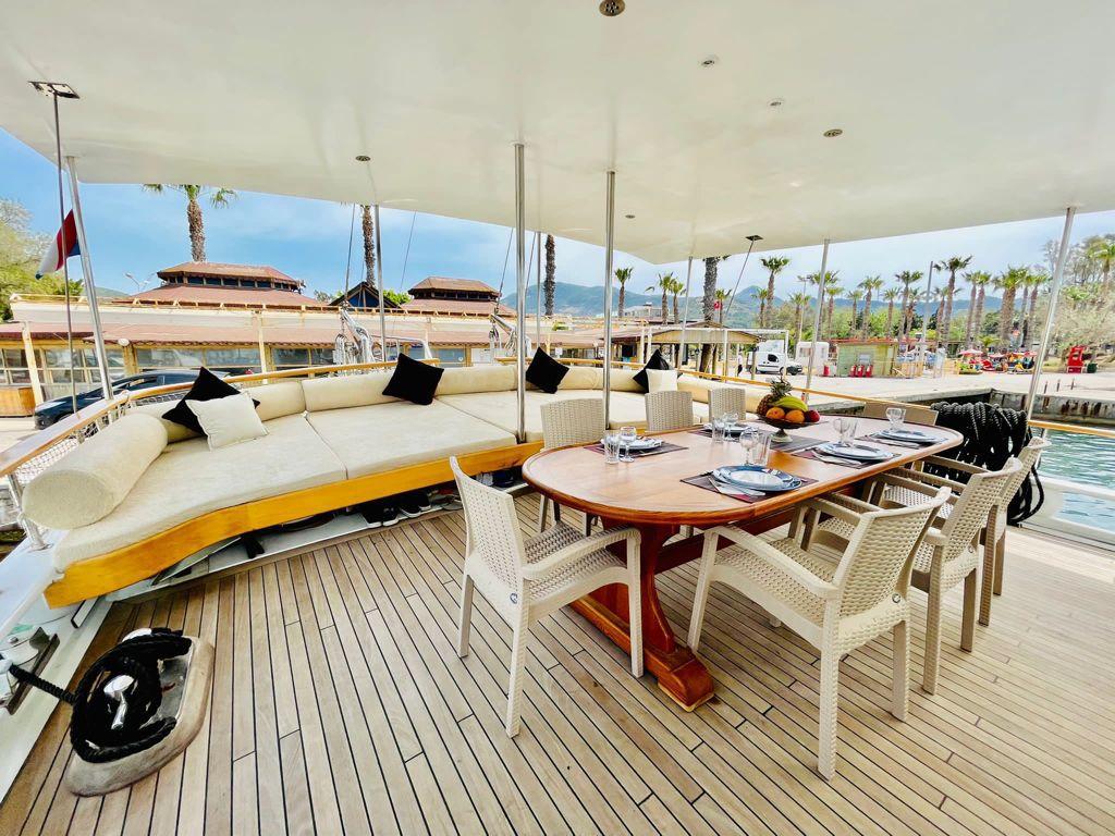 yacht aft deck with oval dining table, wicker chairs, curved seating with cushions under white canopy