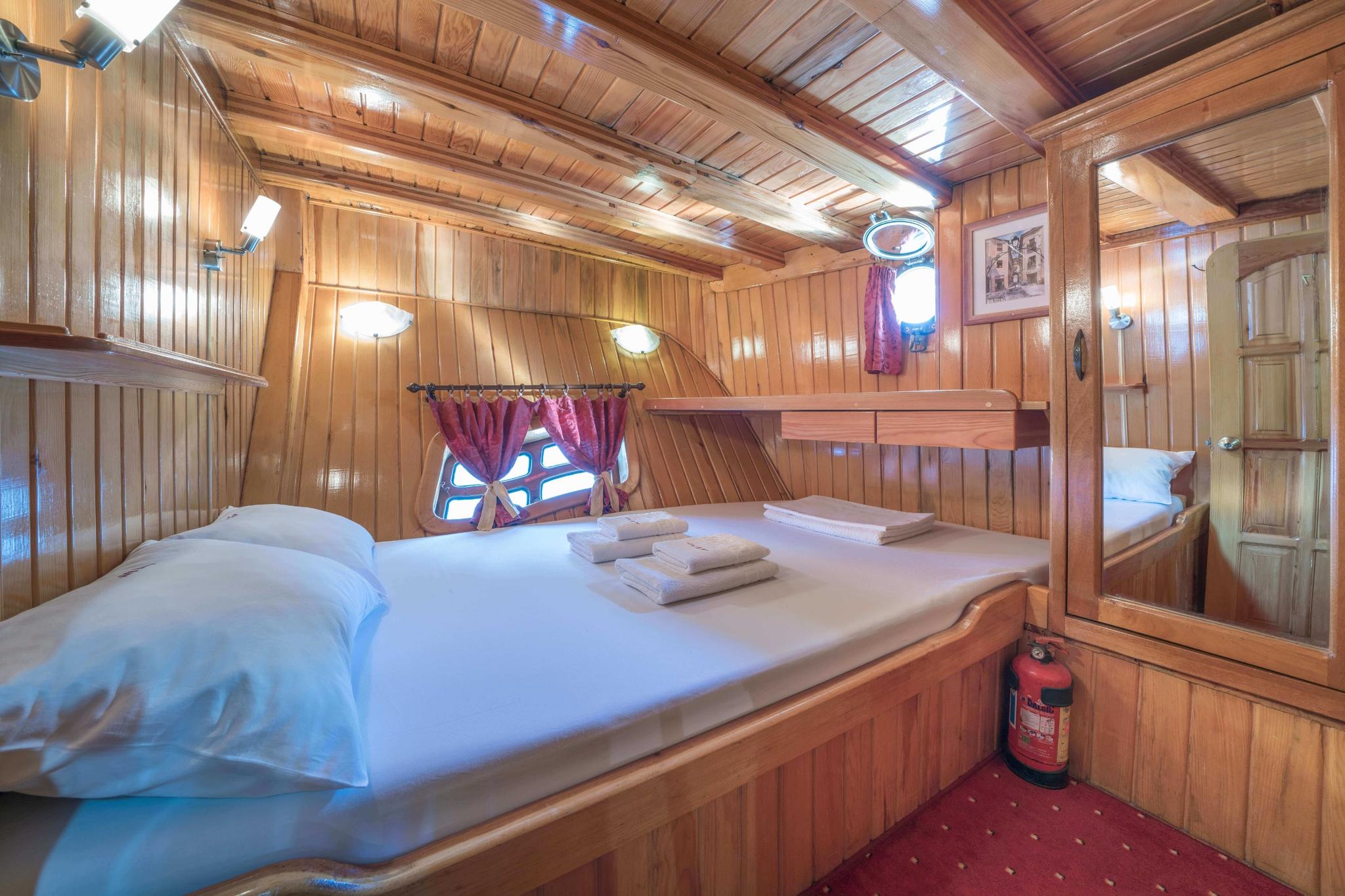 yacht guest cabin with double bed, upper bunk bed, wood paneling and porthole windows