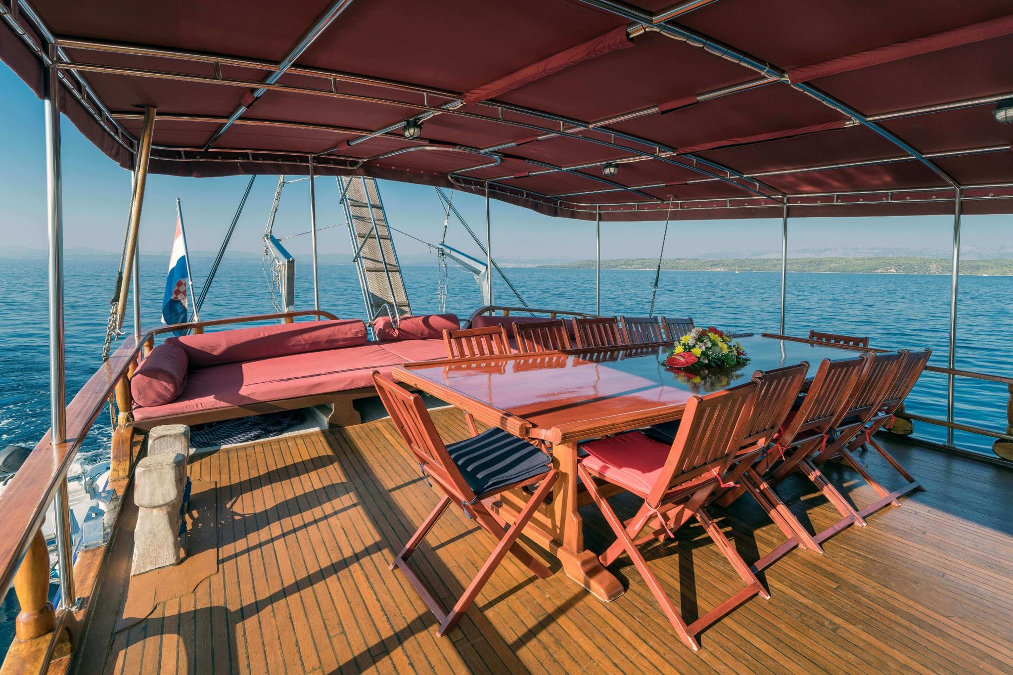 Gulet aft deck dining area with wooden table, red cushioned chairs and built-in seating