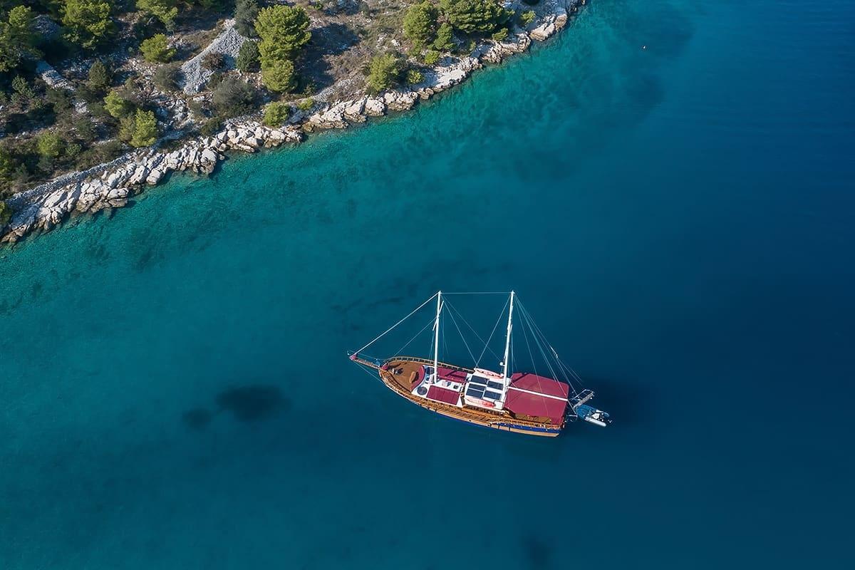 aerial view of traditional wooden gulet yacht anchored in crystal clear turquoise Mediterranean bay