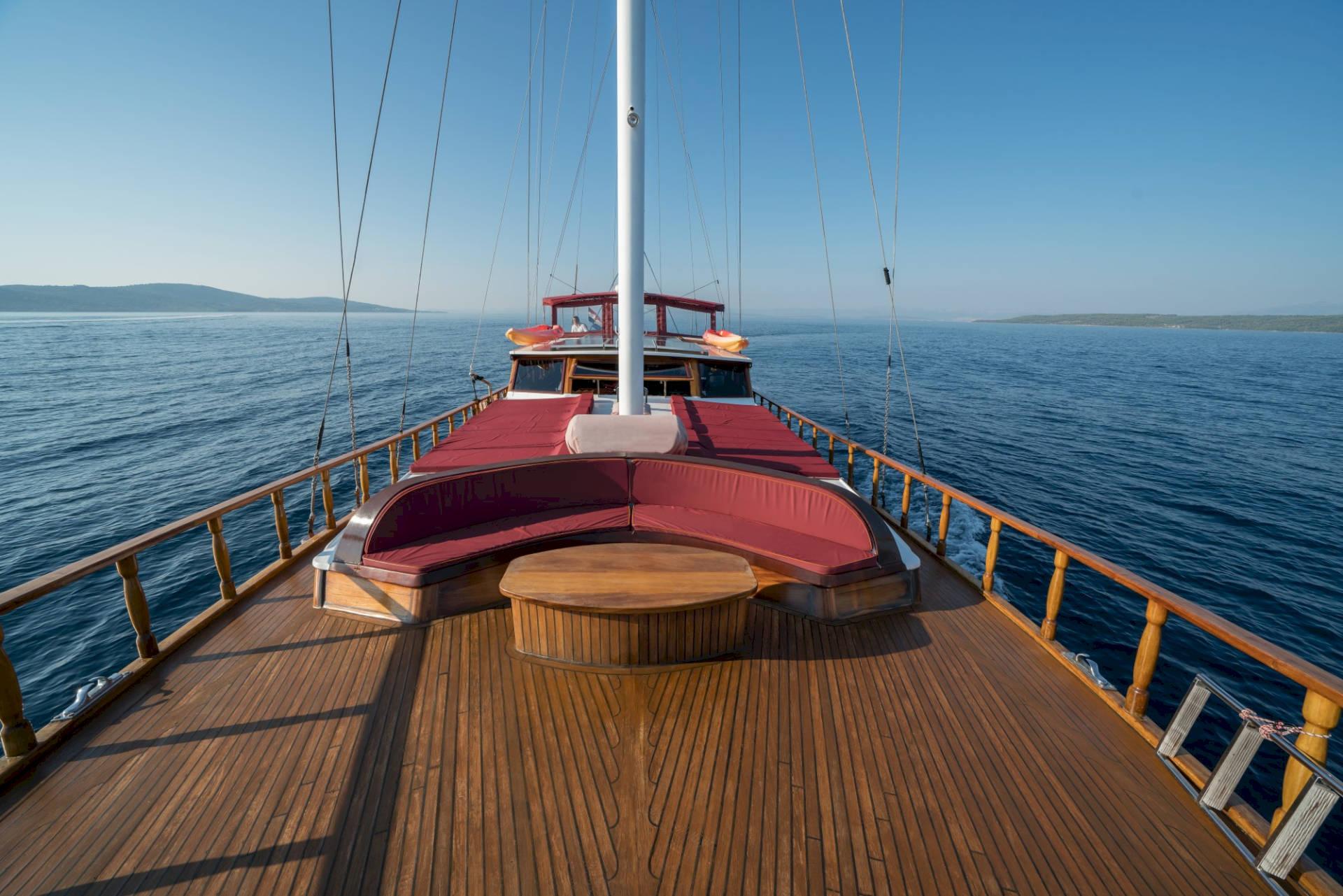 Gulet forward deck with curved red cushioned seating around wooden table and white mast