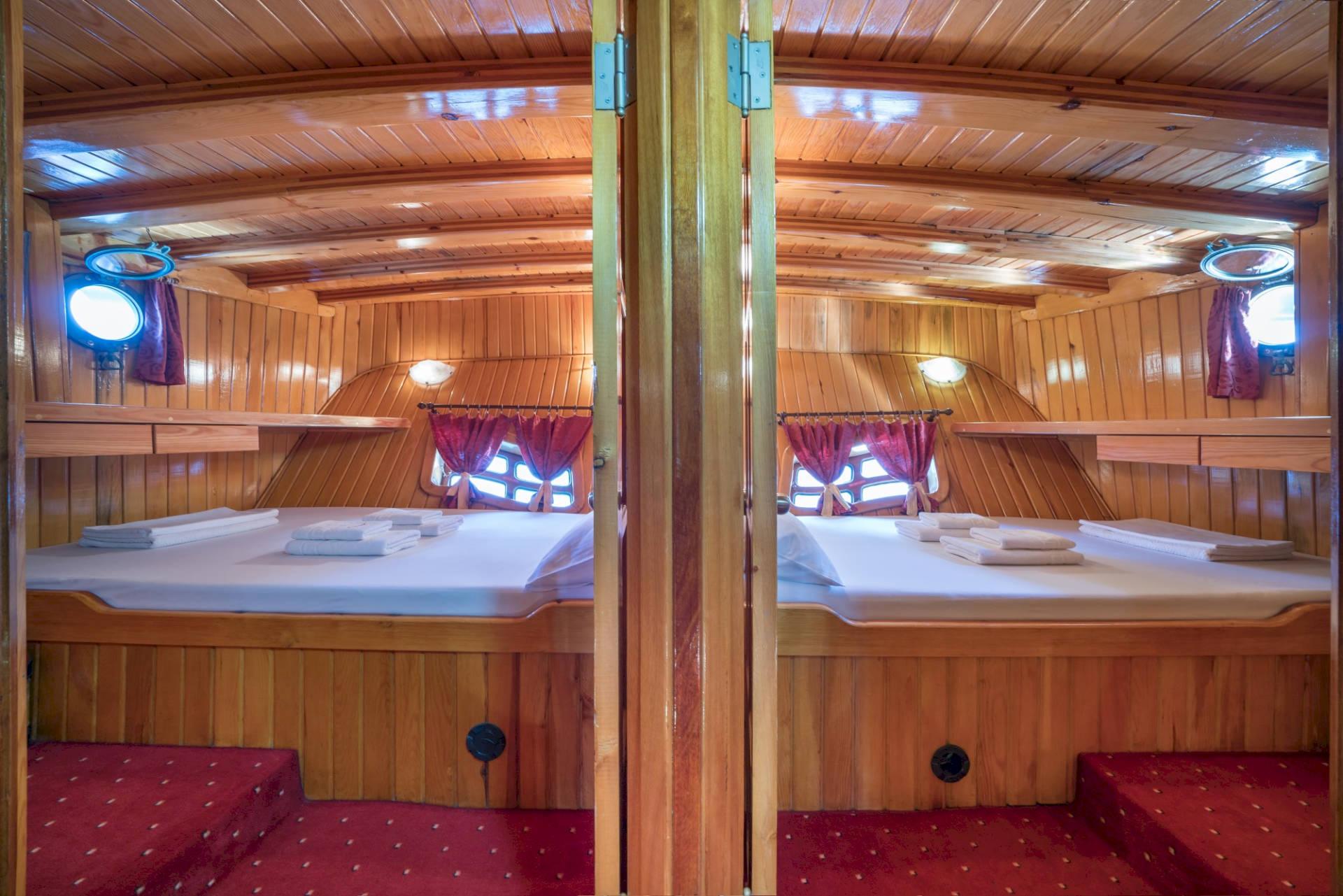 yacht twin cabin interior with wooden bunk beds, red curtains and carpeting