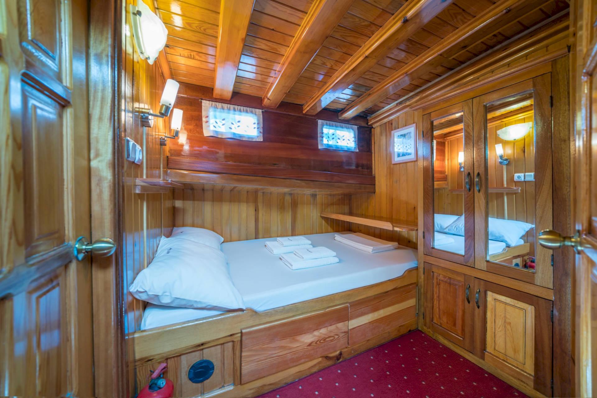 yacht guest cabin with wooden built-in bed, storage cabinets and red carpet flooring