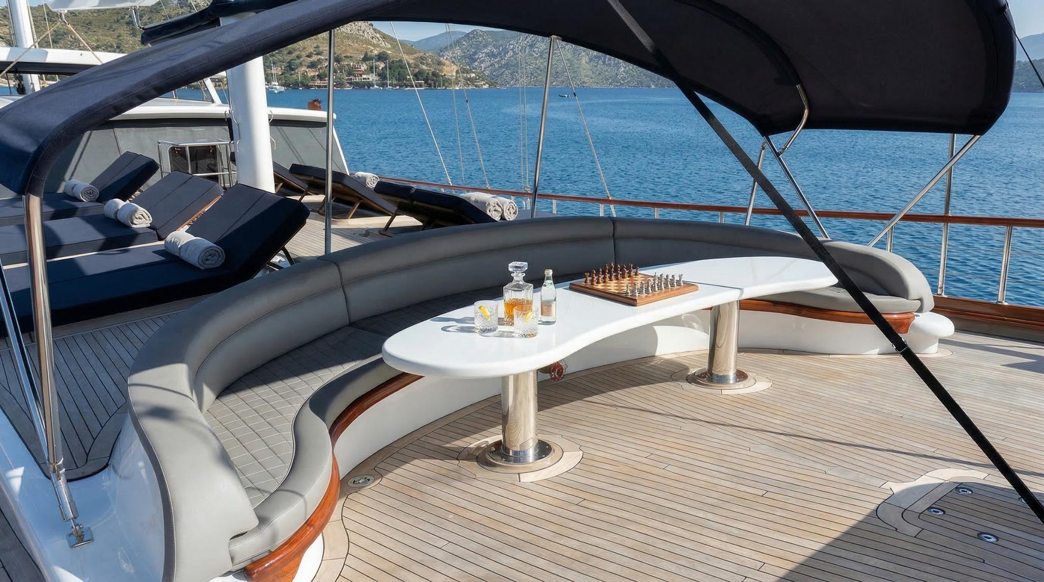 yacht aft deck with curved gray seating, oval white table, chess set and drinks